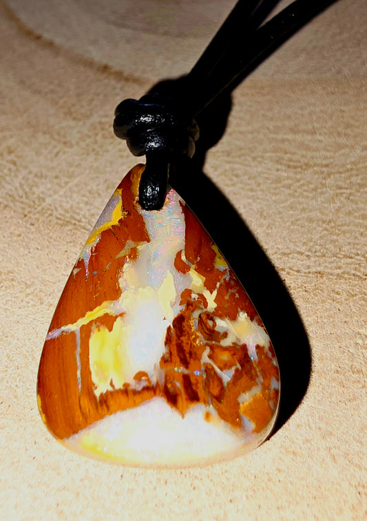 Marbled opal pendant on a black cord against a beige background