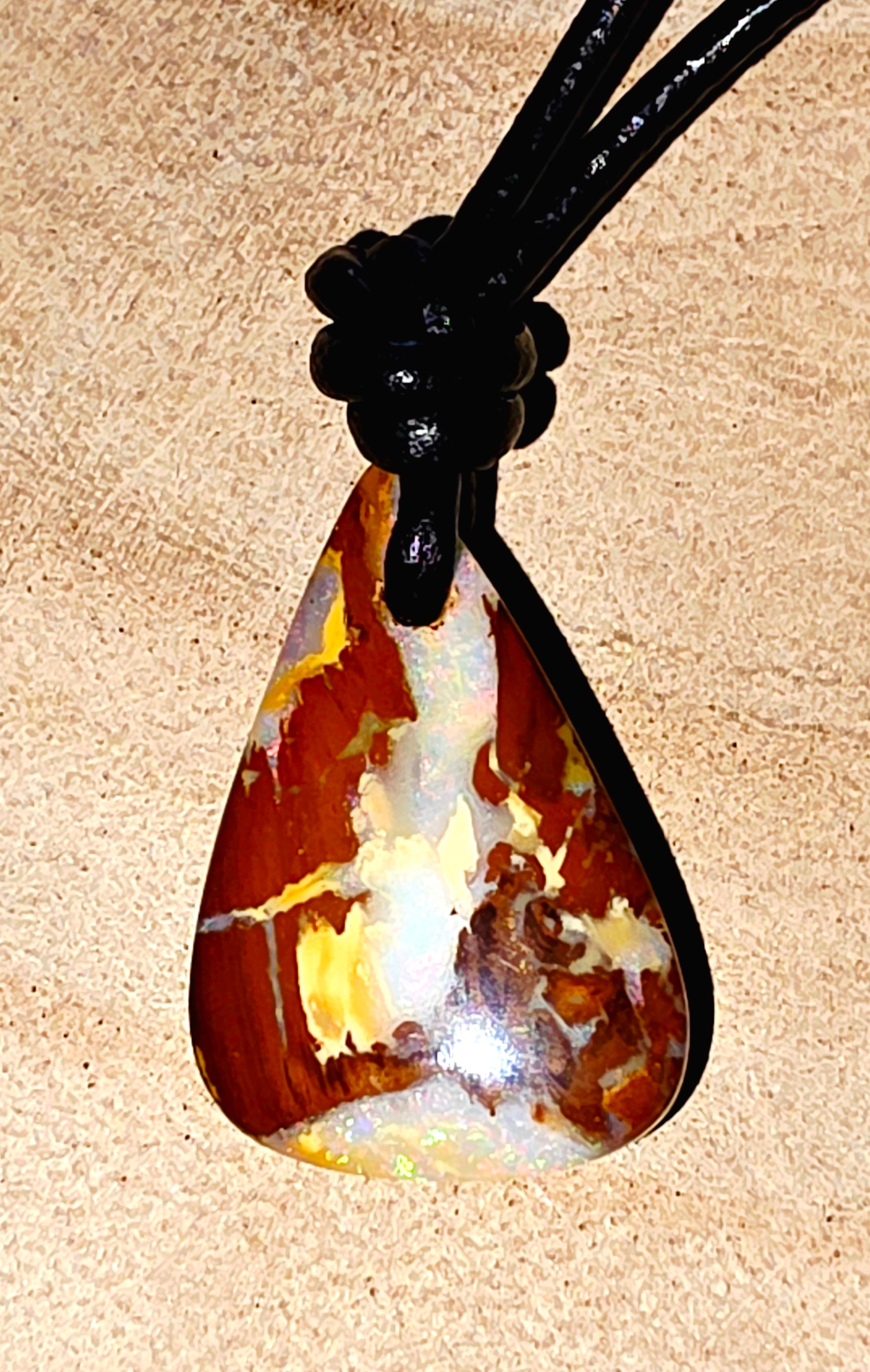 Teardrop-shaped opal pendant on a black cord against a beige background