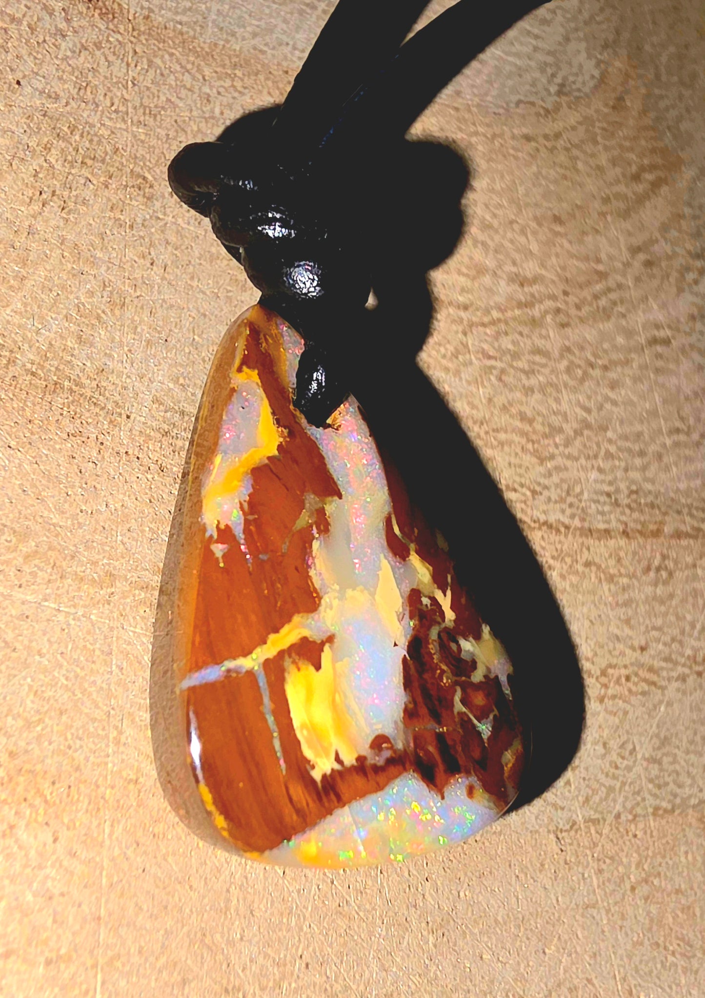 Opal pendant on a black cord against a beige background