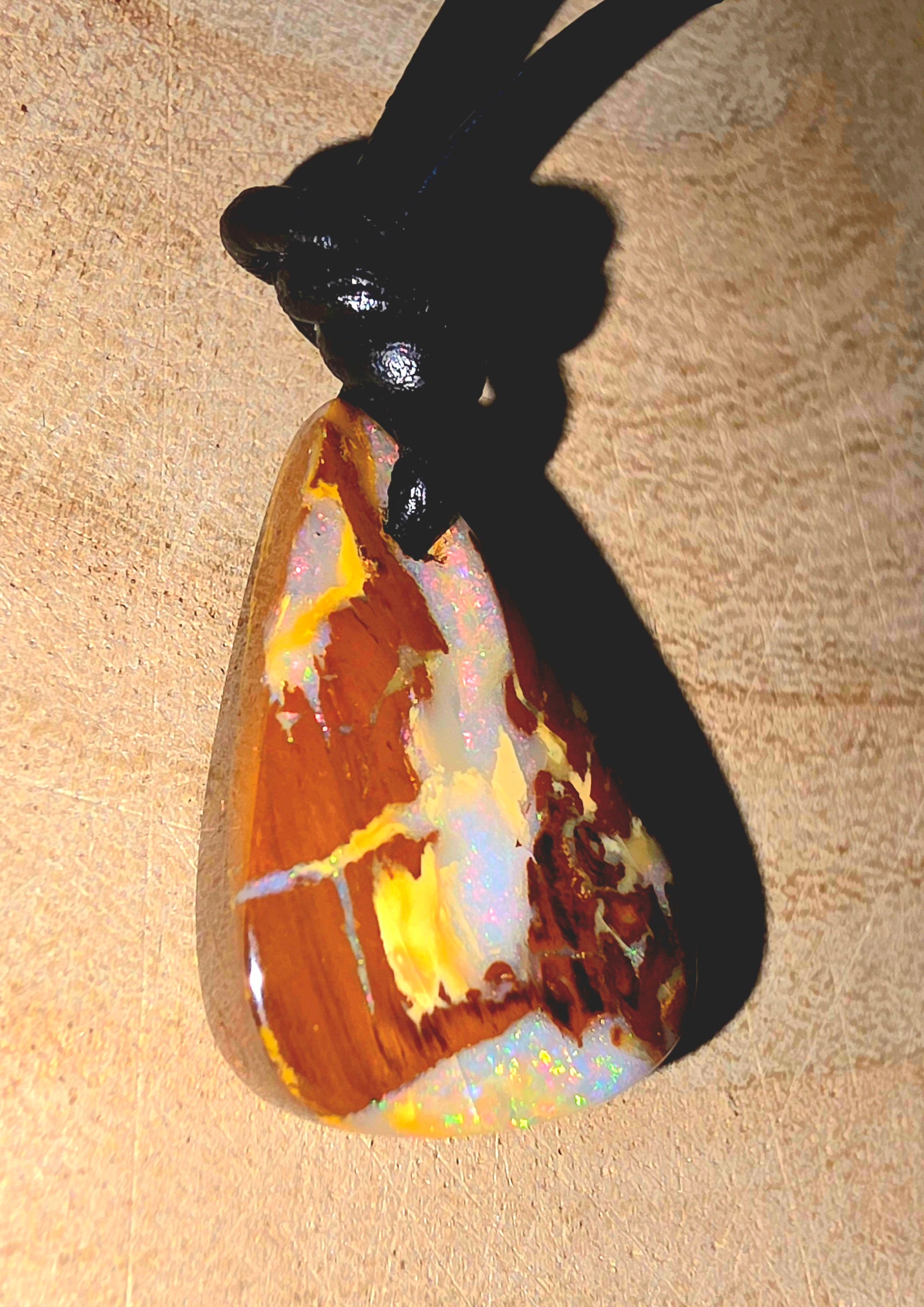 Opal pendant on a black cord against a beige background