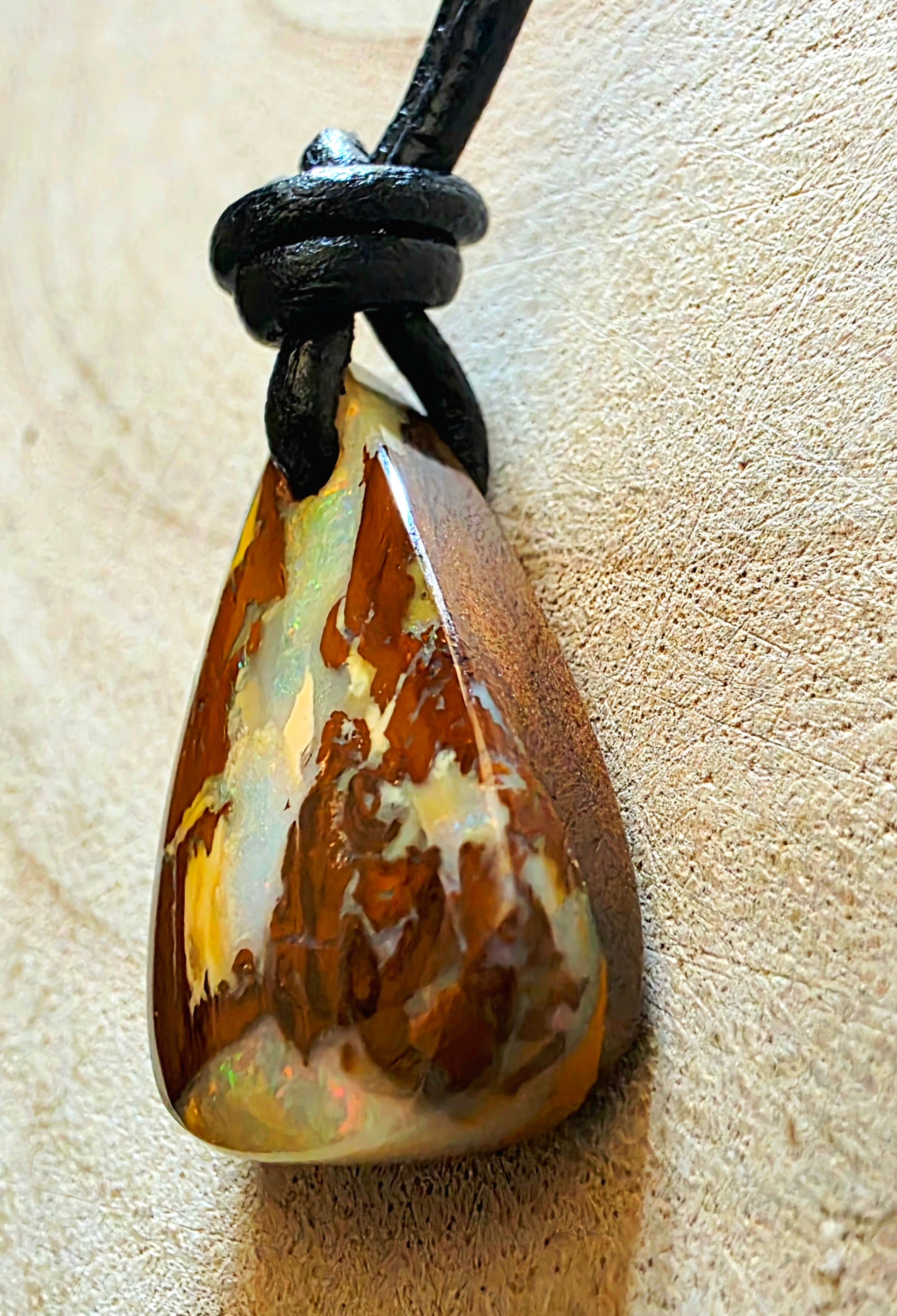 Opal pendant on a black cord against a beige background