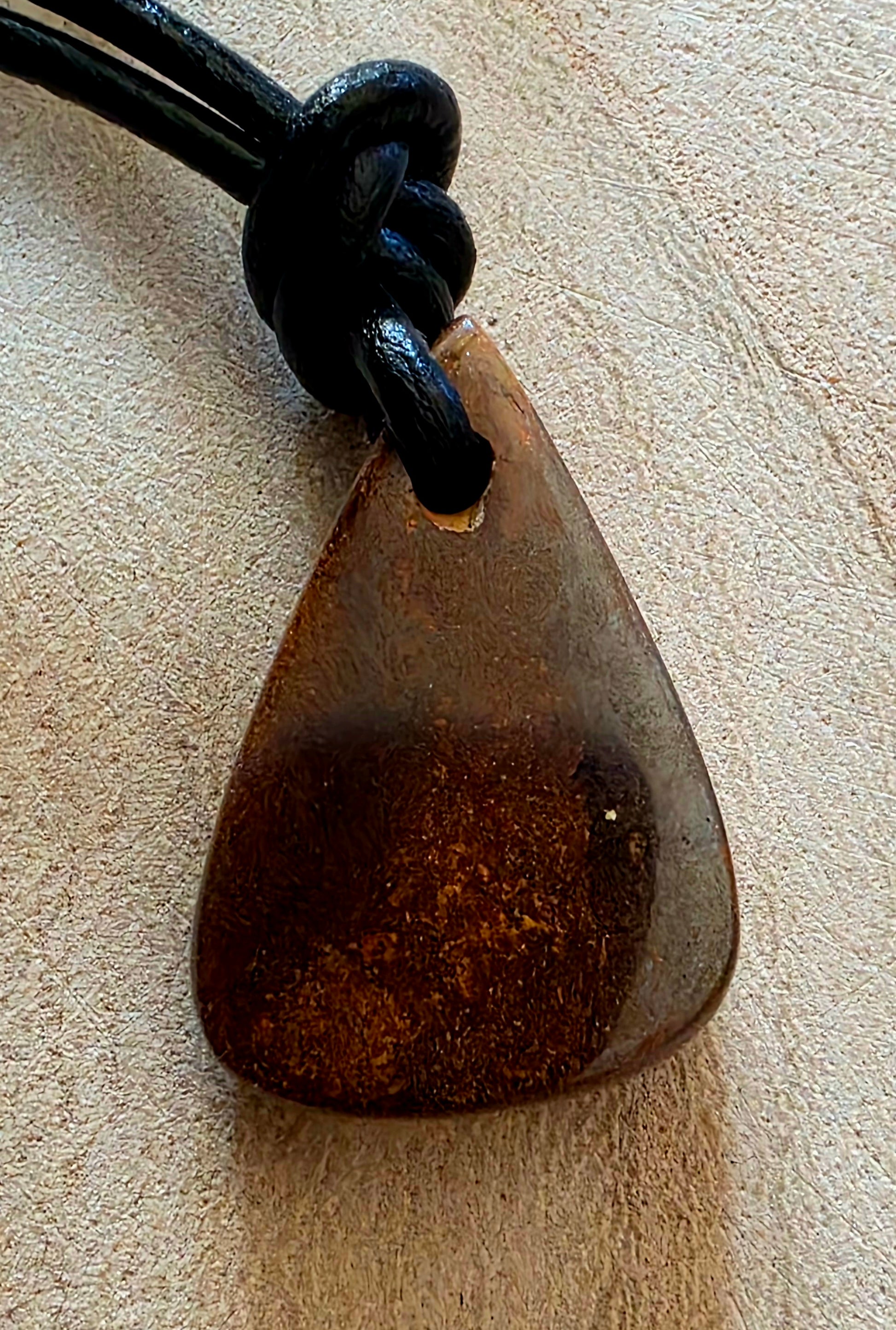 Brown pendant on a black cord against a beige background
