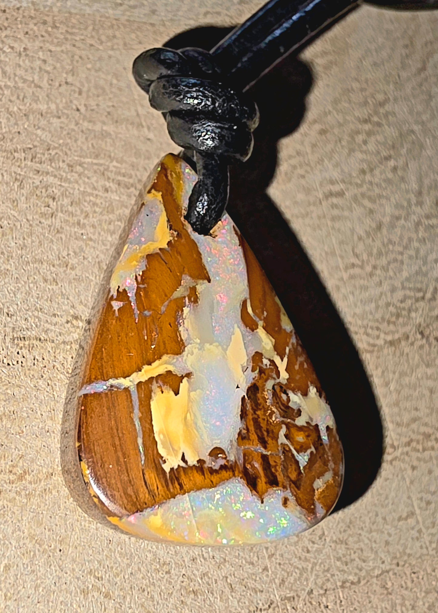 Opal pendant with a black cord on a beige background