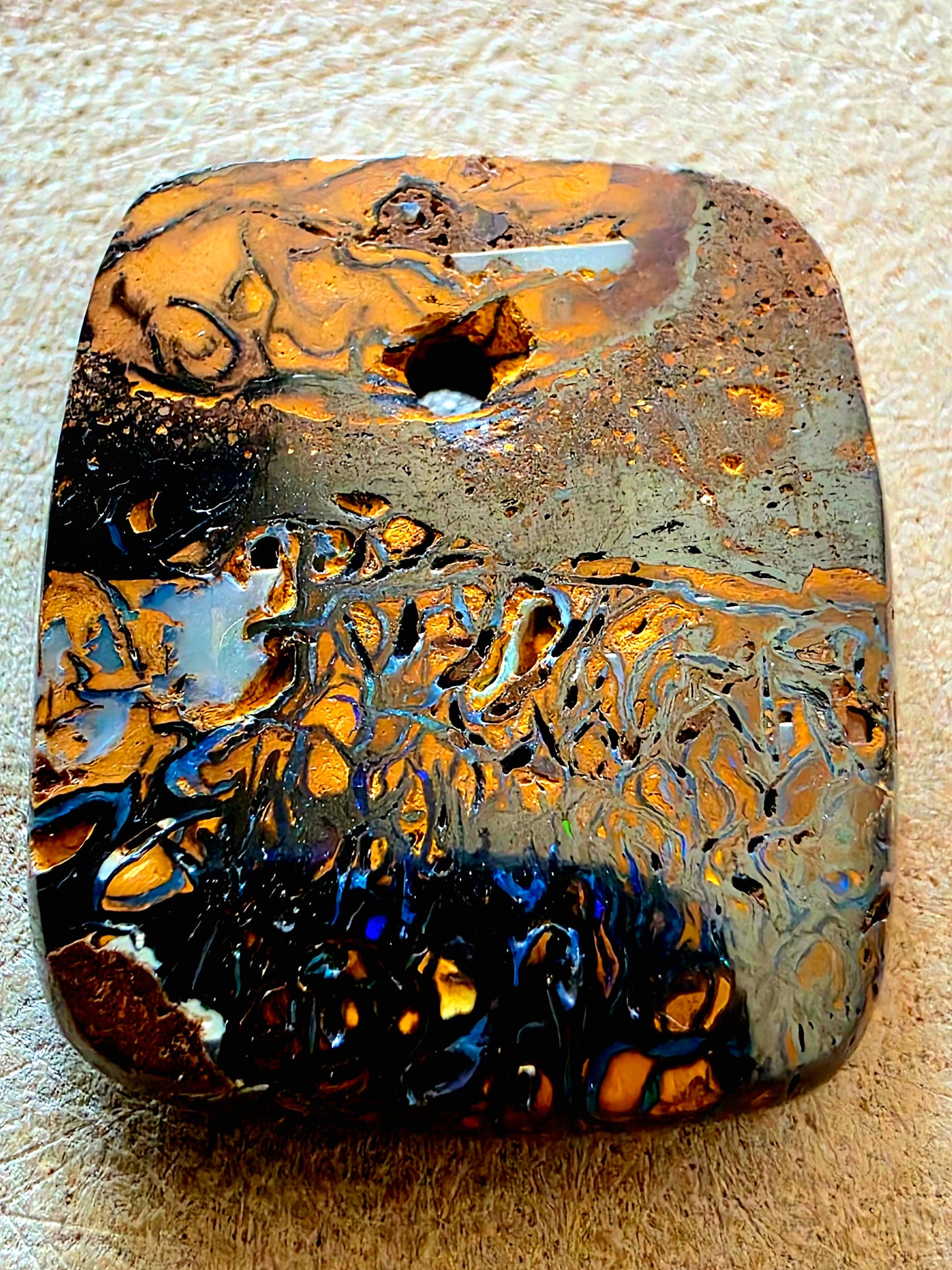 Rust-coloured opal stone with intricate patterns on a beige background