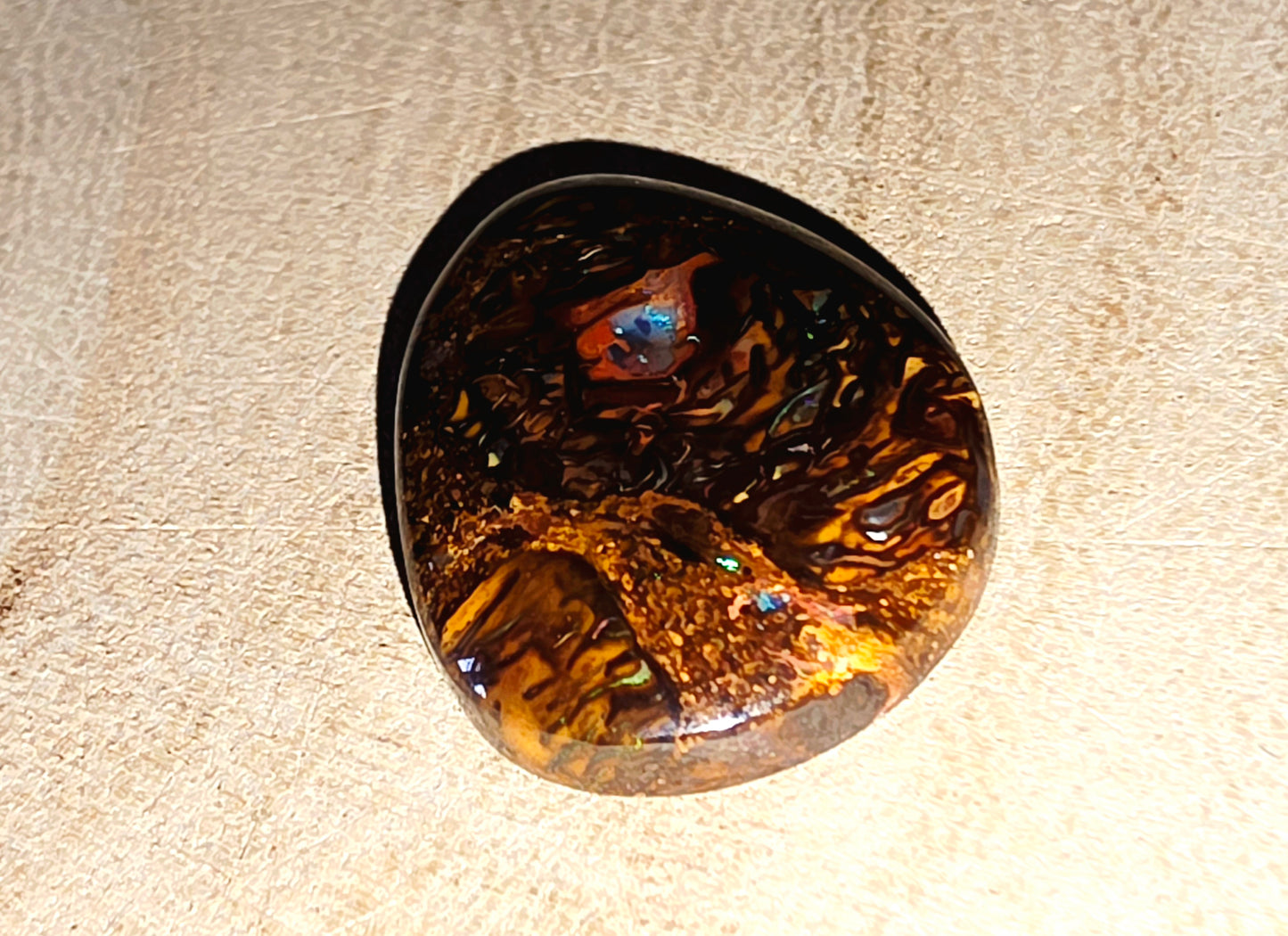 Round opal stone with a tiger's eye pattern on a beige surface