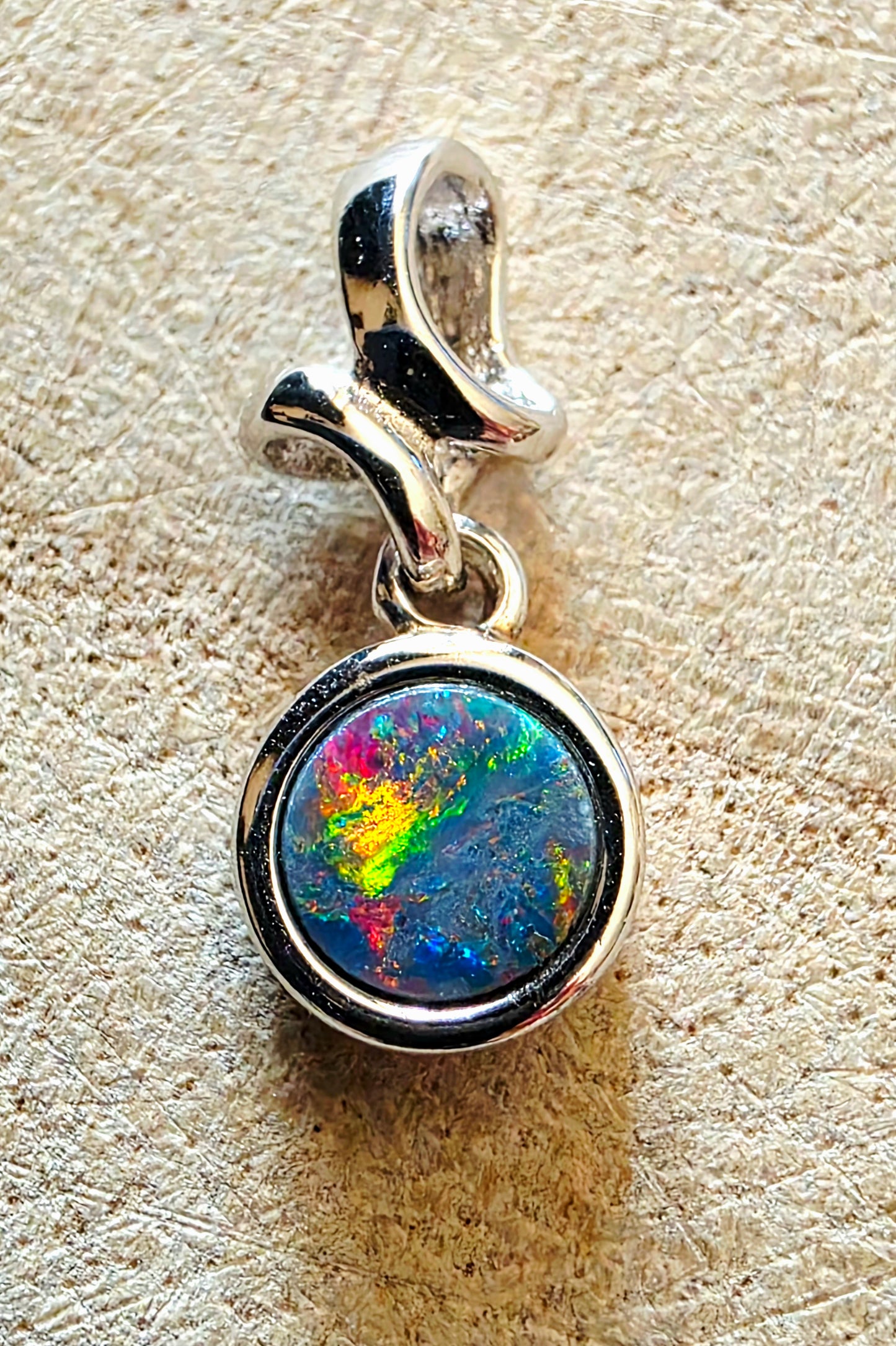 Silver pendant with a colourful gemstone on a textured beige background