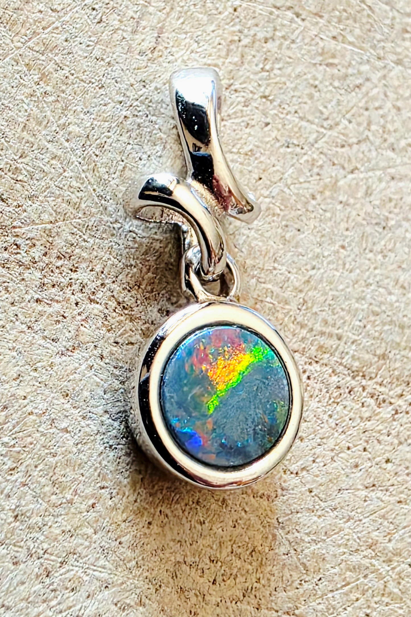 Silver pendant with a colourful gemstone on a textured beige surface