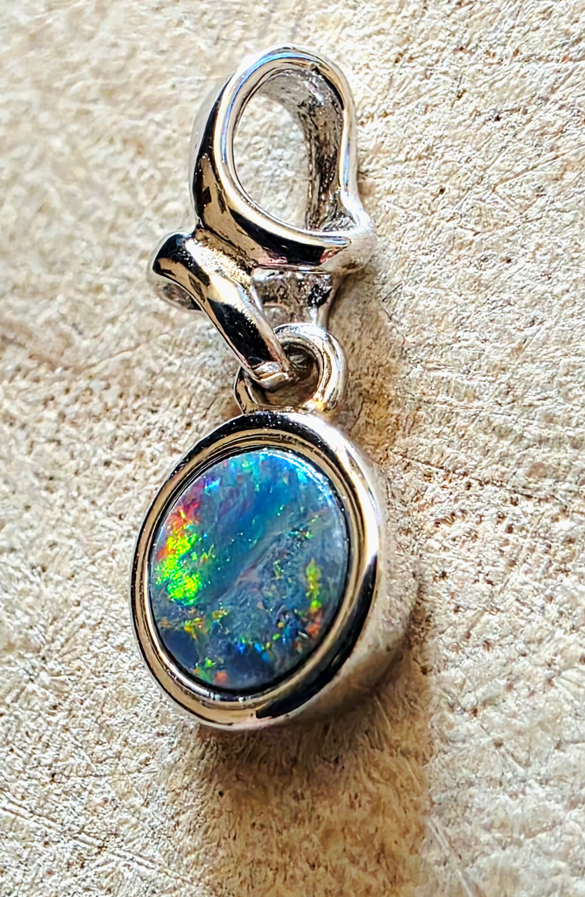 Silver pendant with a colourful gemstone on a textured beige background