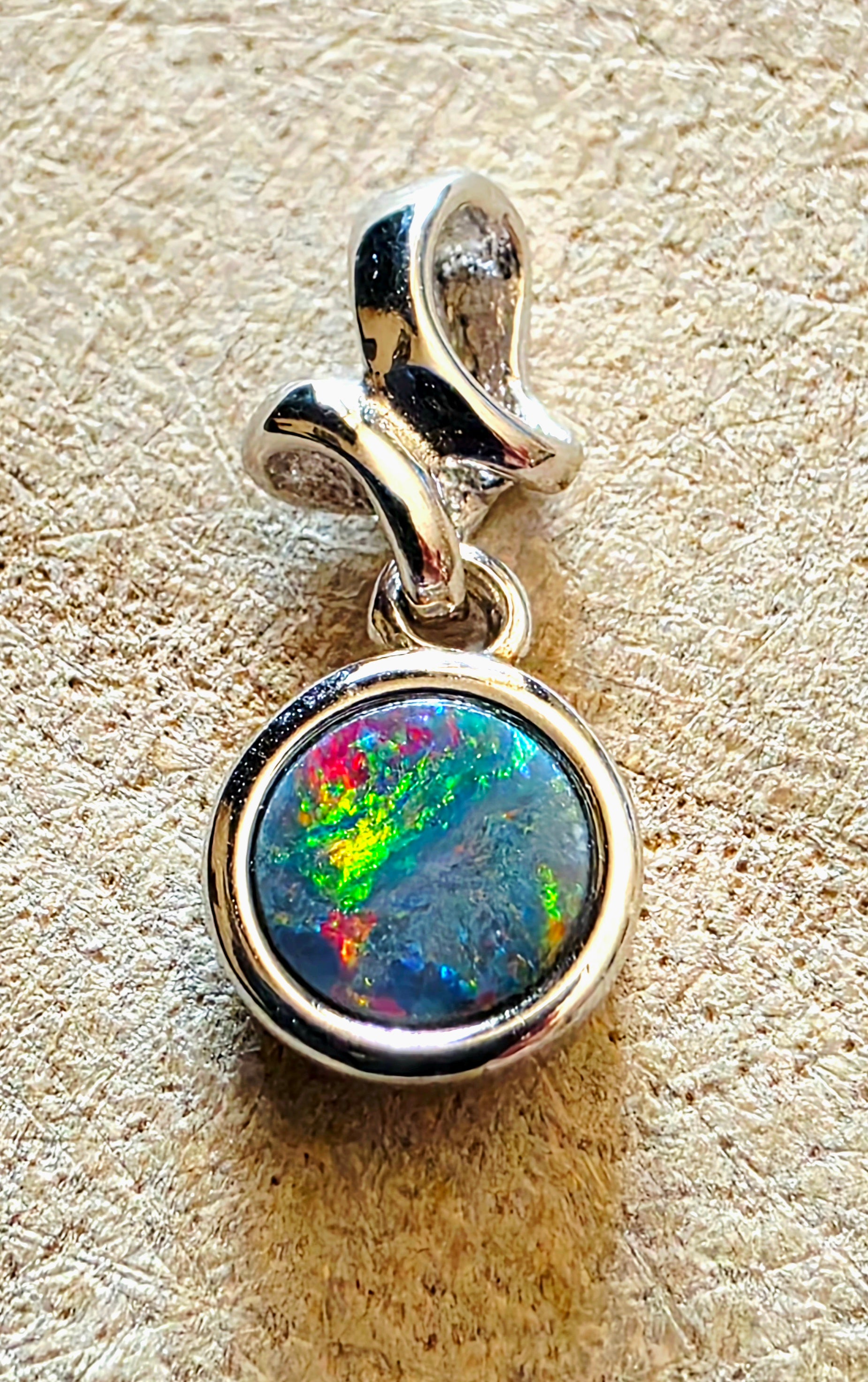 Silver pendant with a colourful opal gemstone on a textured beige background