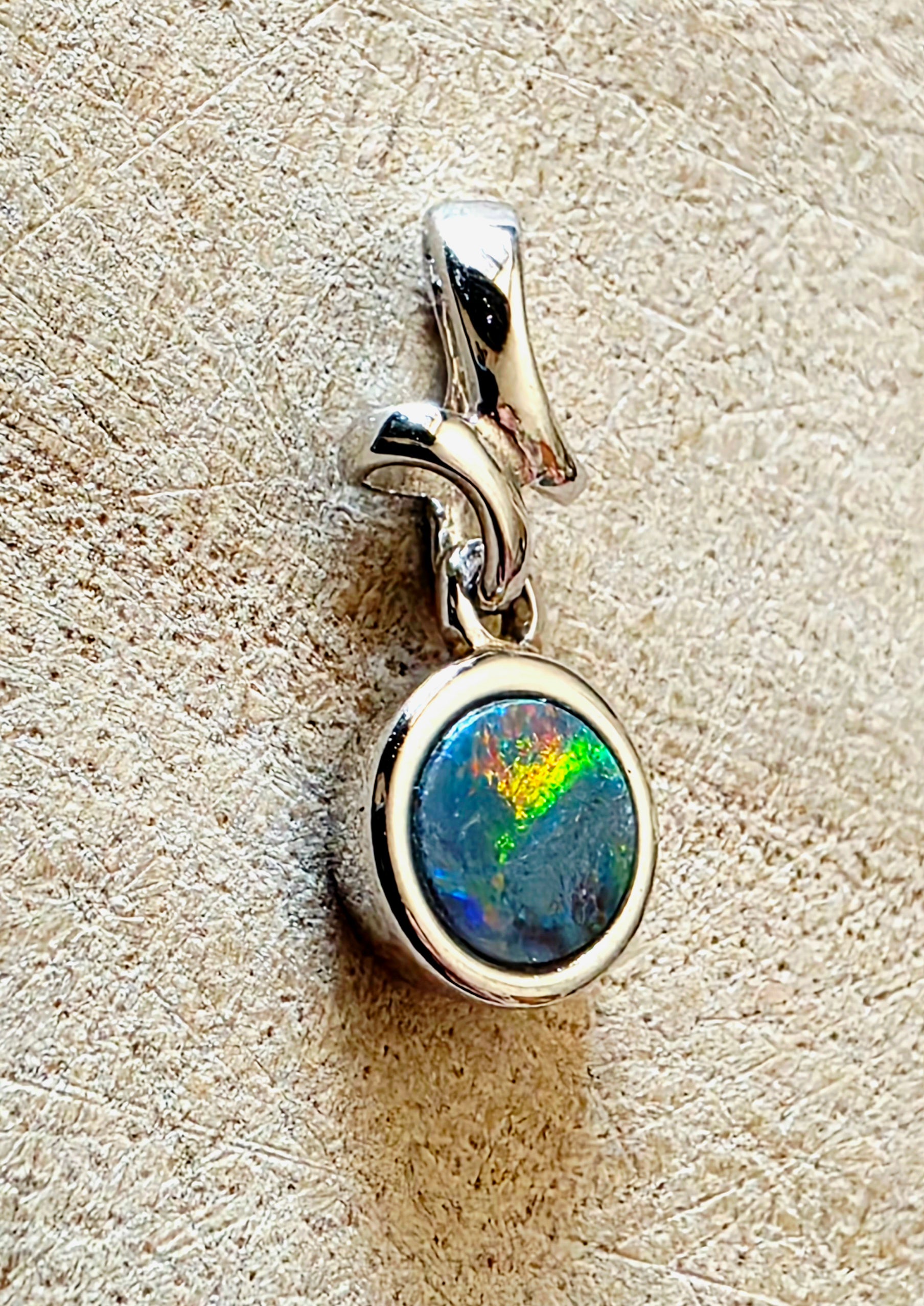 Silver pendant with a colourful gemstone on a textured beige background