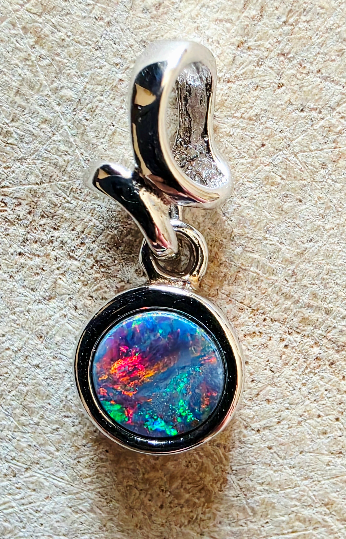 Silver pendant with a colourful opal gemstone on a textured beige background