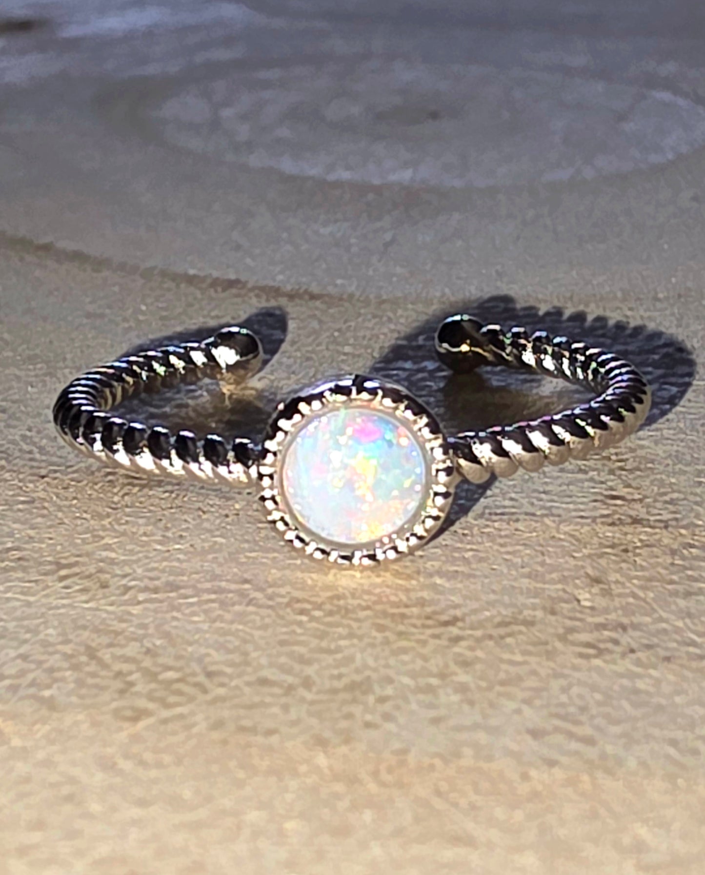 Silver ring with a central opal stone on a sandy background