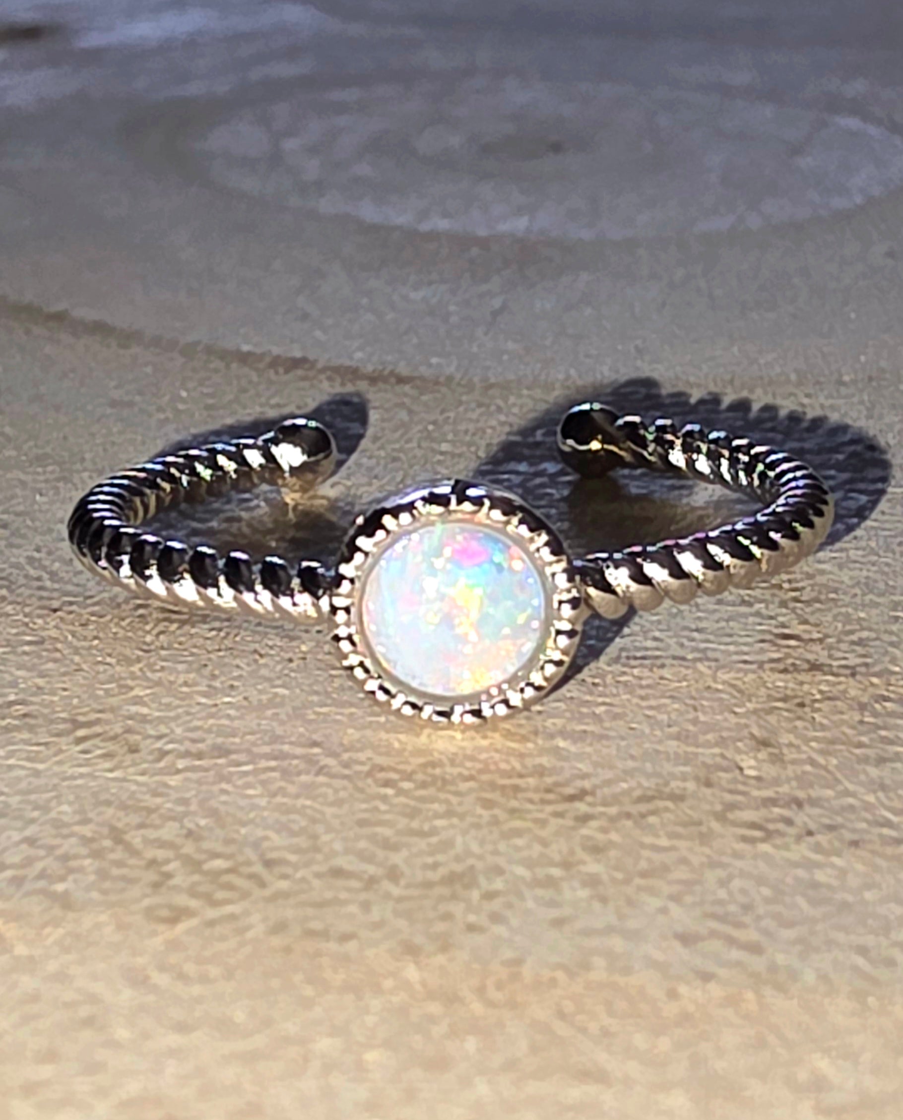 Silver ring with a central opal stone on a sandy background