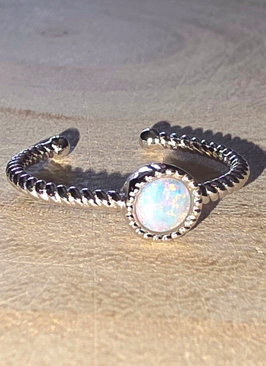 Silver ring with a central opal stone on a textured beige surface