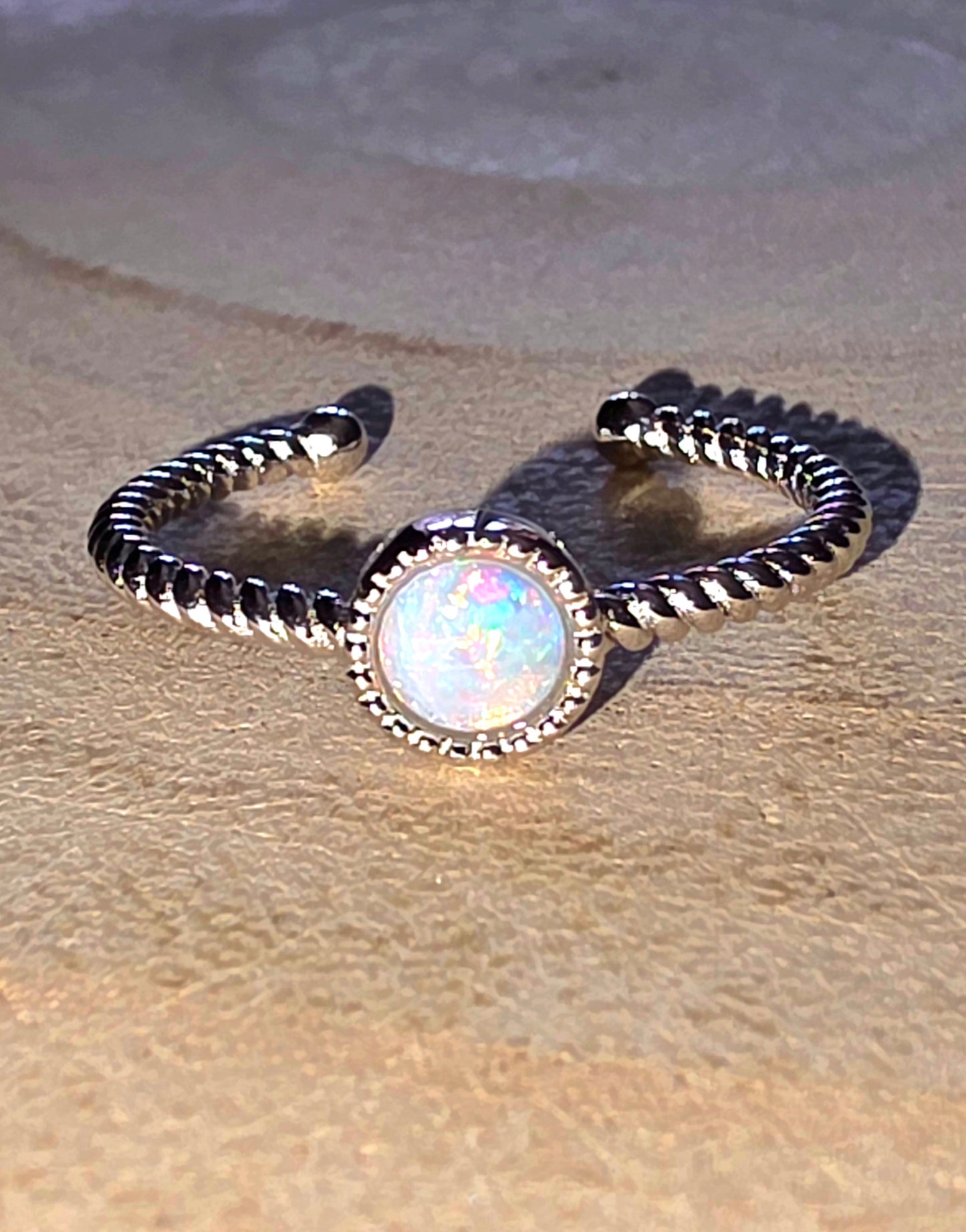 Silver ring with a central opal stone on a textured beige surface