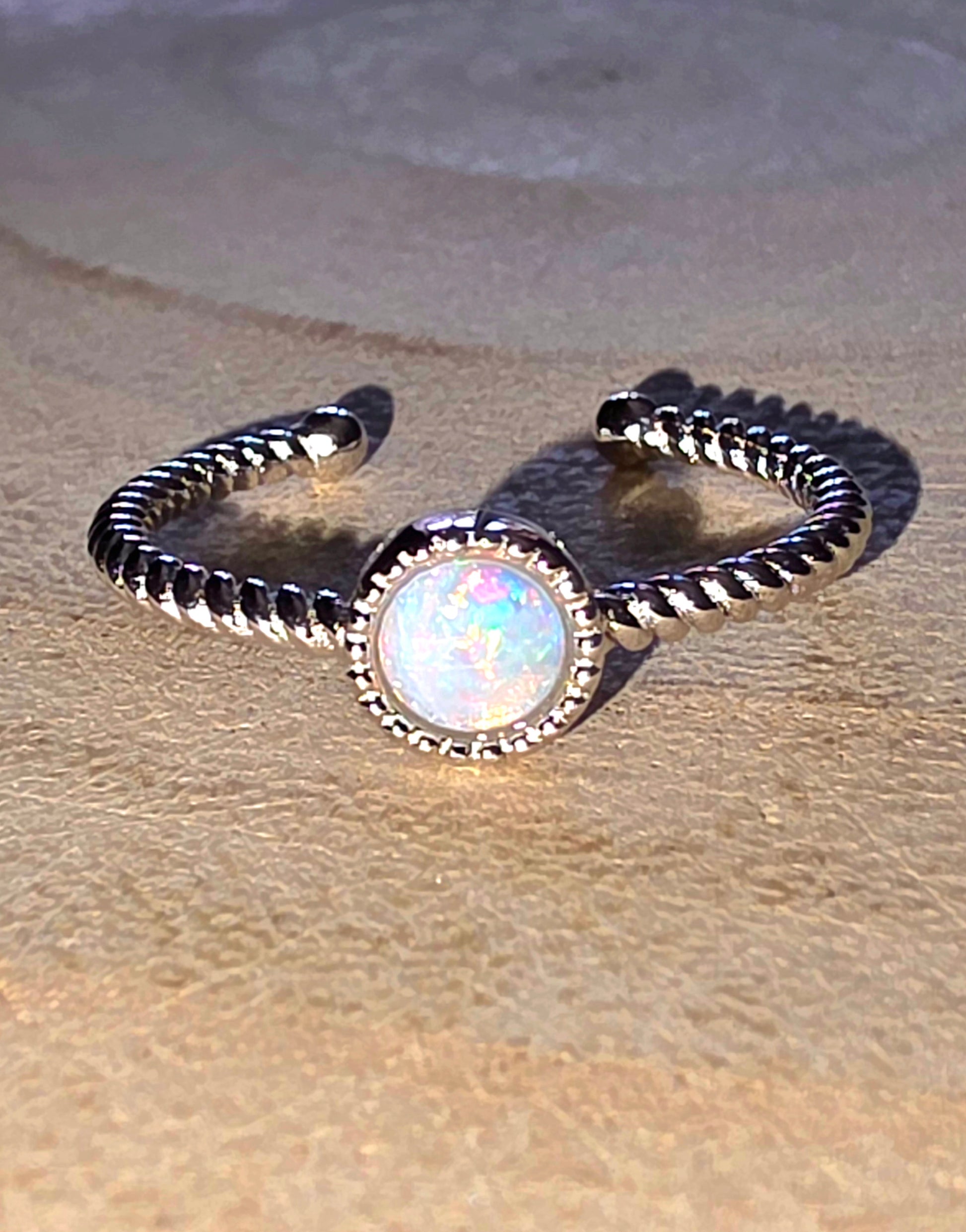 Silver ring with a central opal stone on a textured beige surface