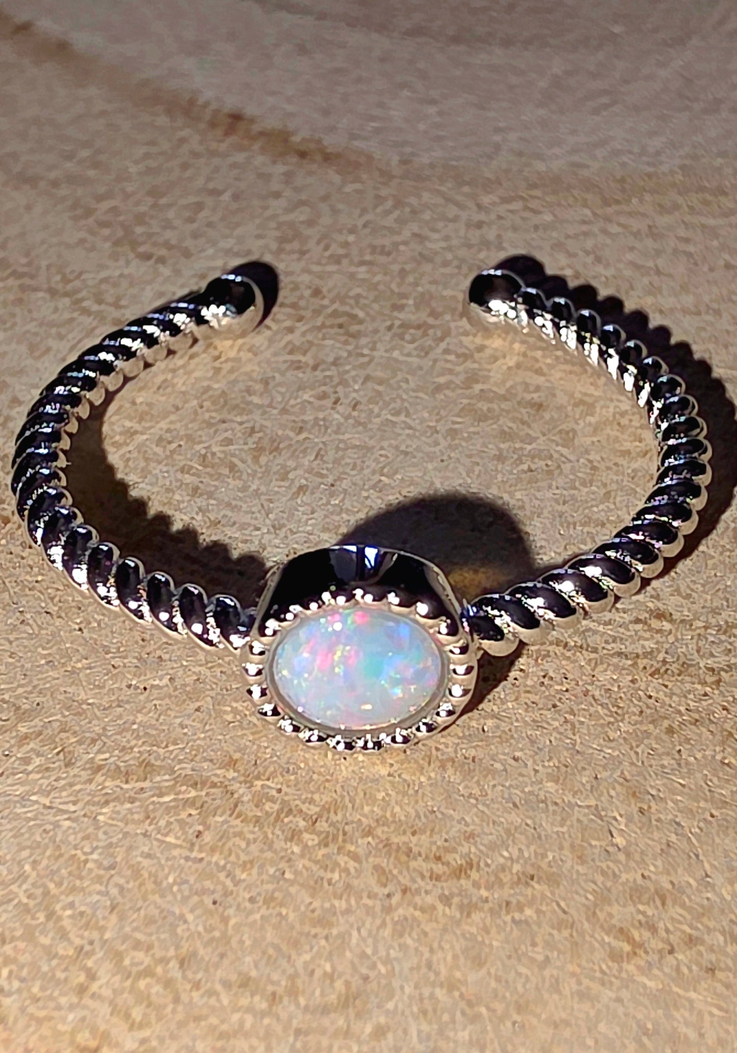 Silver ring with a central opal stone on a beige surface