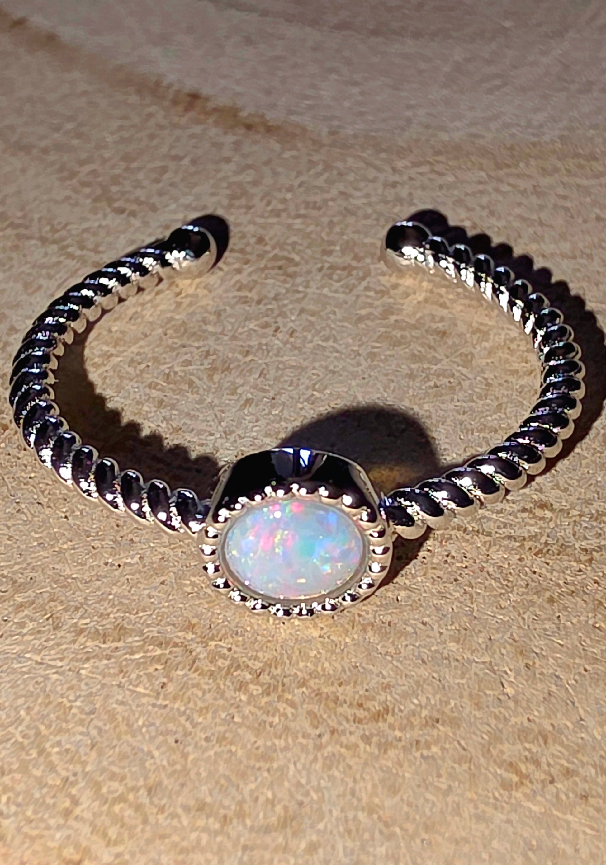 Silver ring with a central opal stone on a beige surface