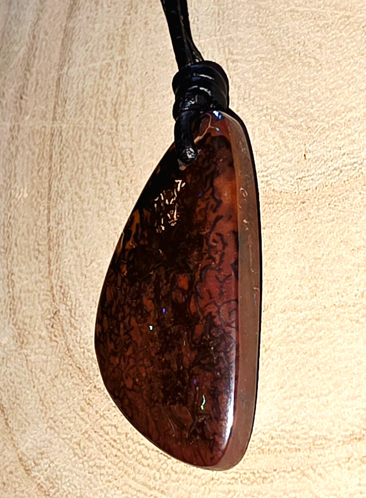 Brown opal pendant on a black cord against a beige background