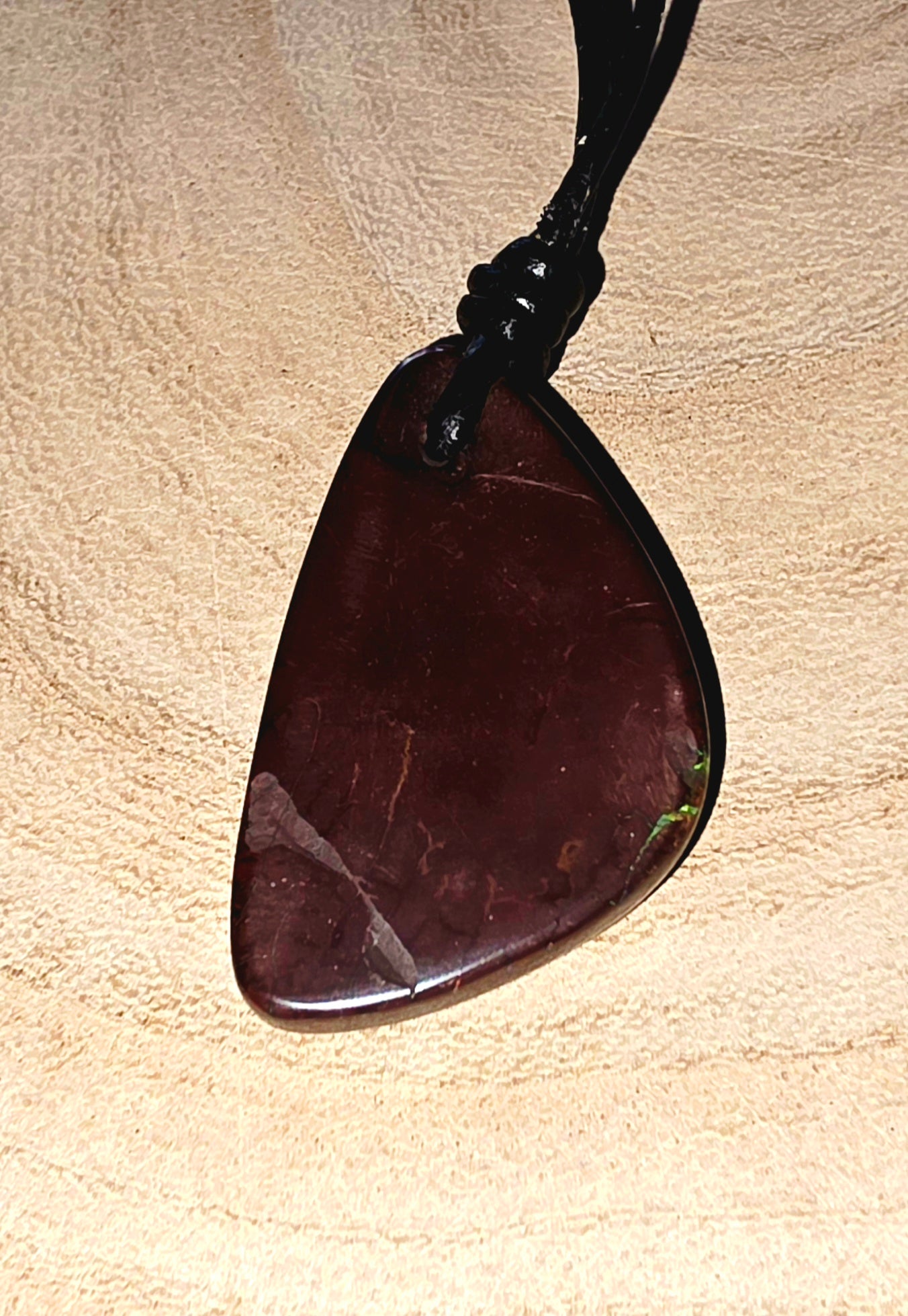 Brown opal pendant on a black cord against a beige background