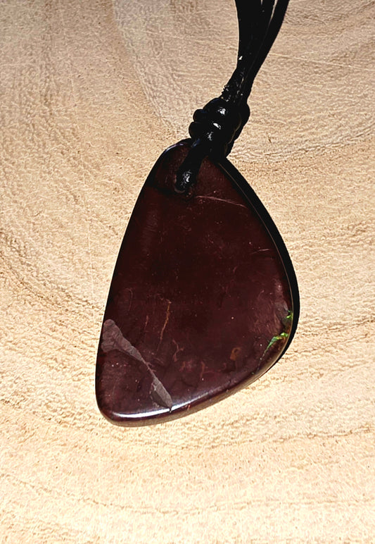 Brown opal pendant on a black cord against a beige background