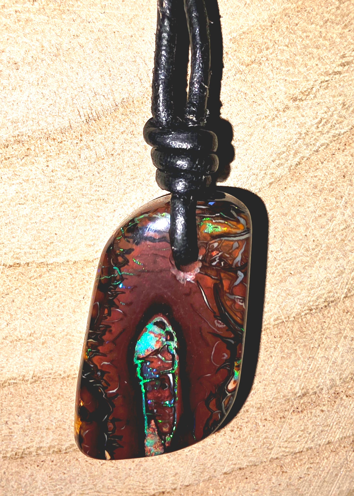Multicoloured pendant on a black cord against a beige background