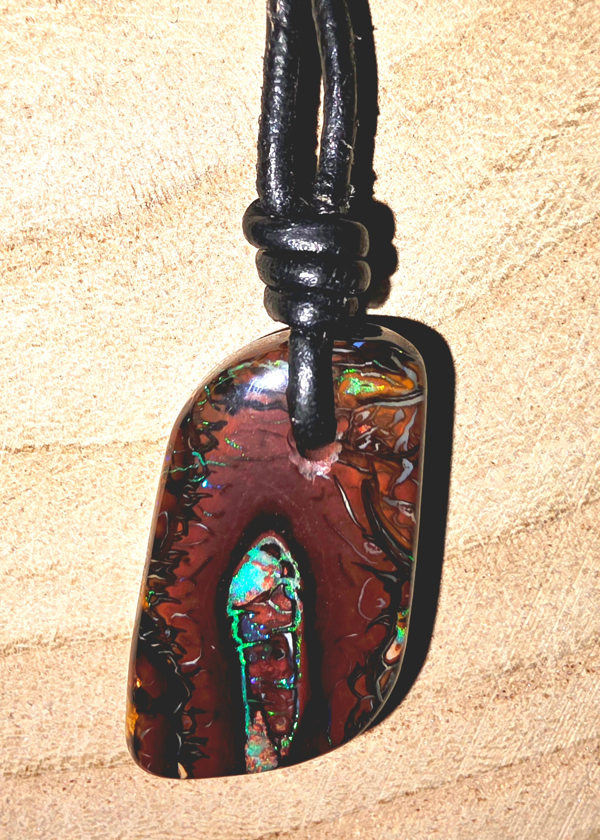 Multicoloured pendant on a black cord against a beige background