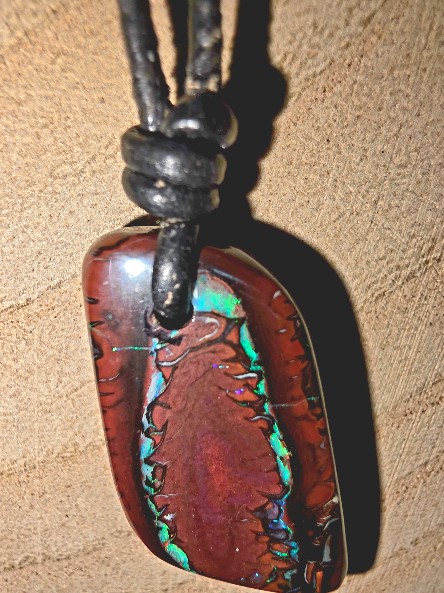 Multicolored stone pendant on a leather cord against a beige background