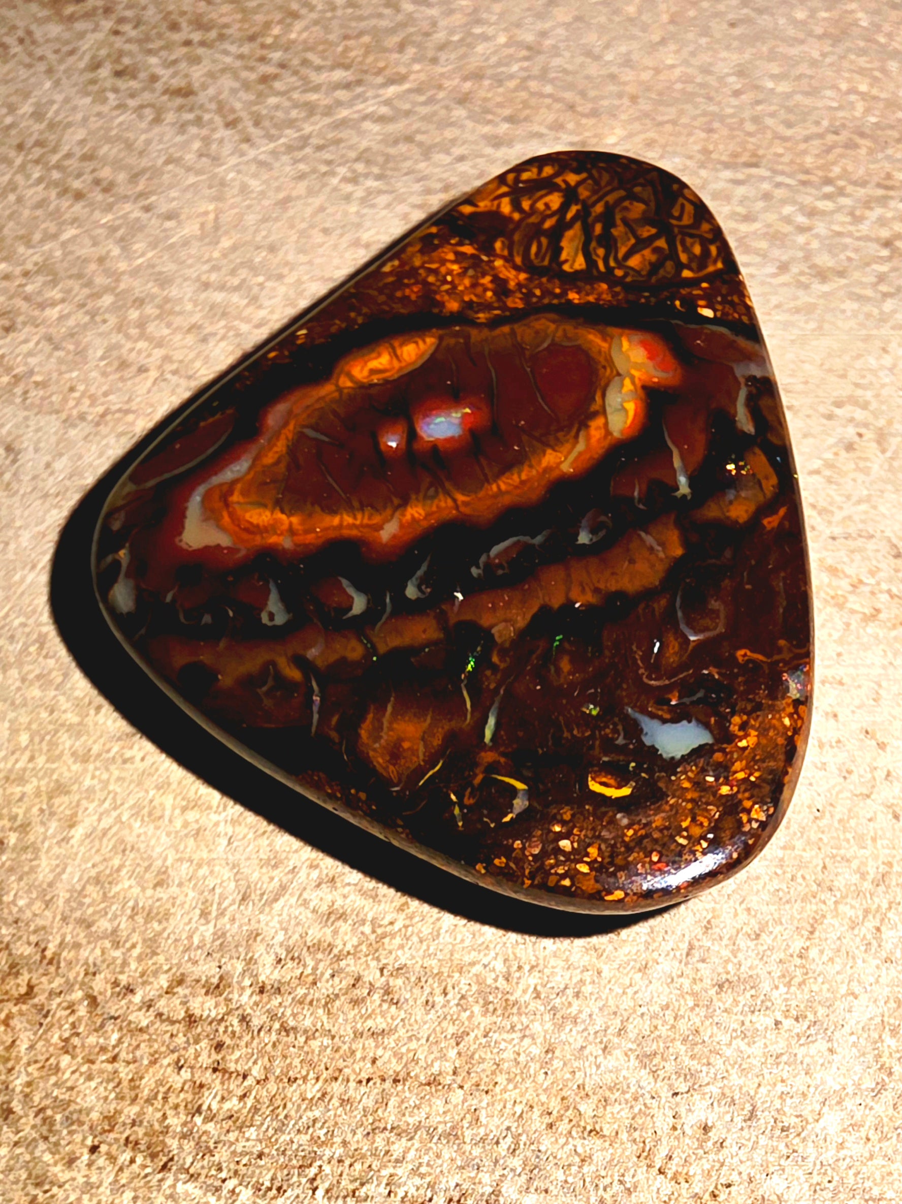 Polished piece of boulder opal on a beige surface