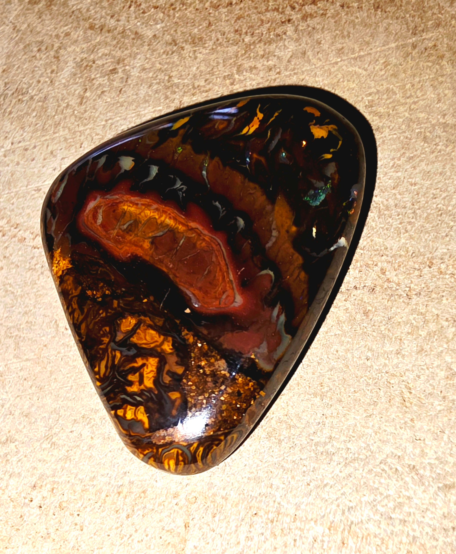 Triangular polished stone with brown and black patterns on a beige surface