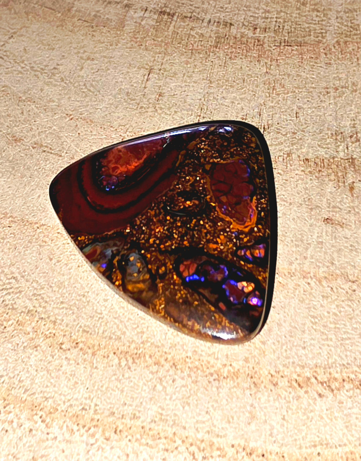 Polished boulder opal with iridescent surface on a beige background