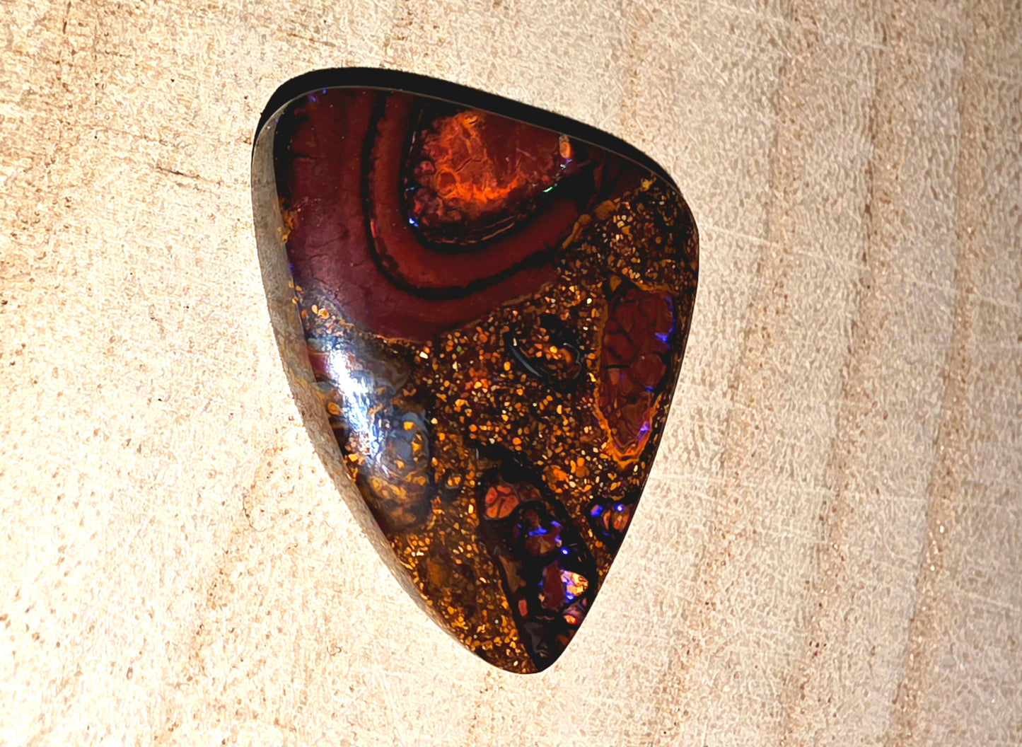 Polished opal stone with brown and purple patterns on a beige surface