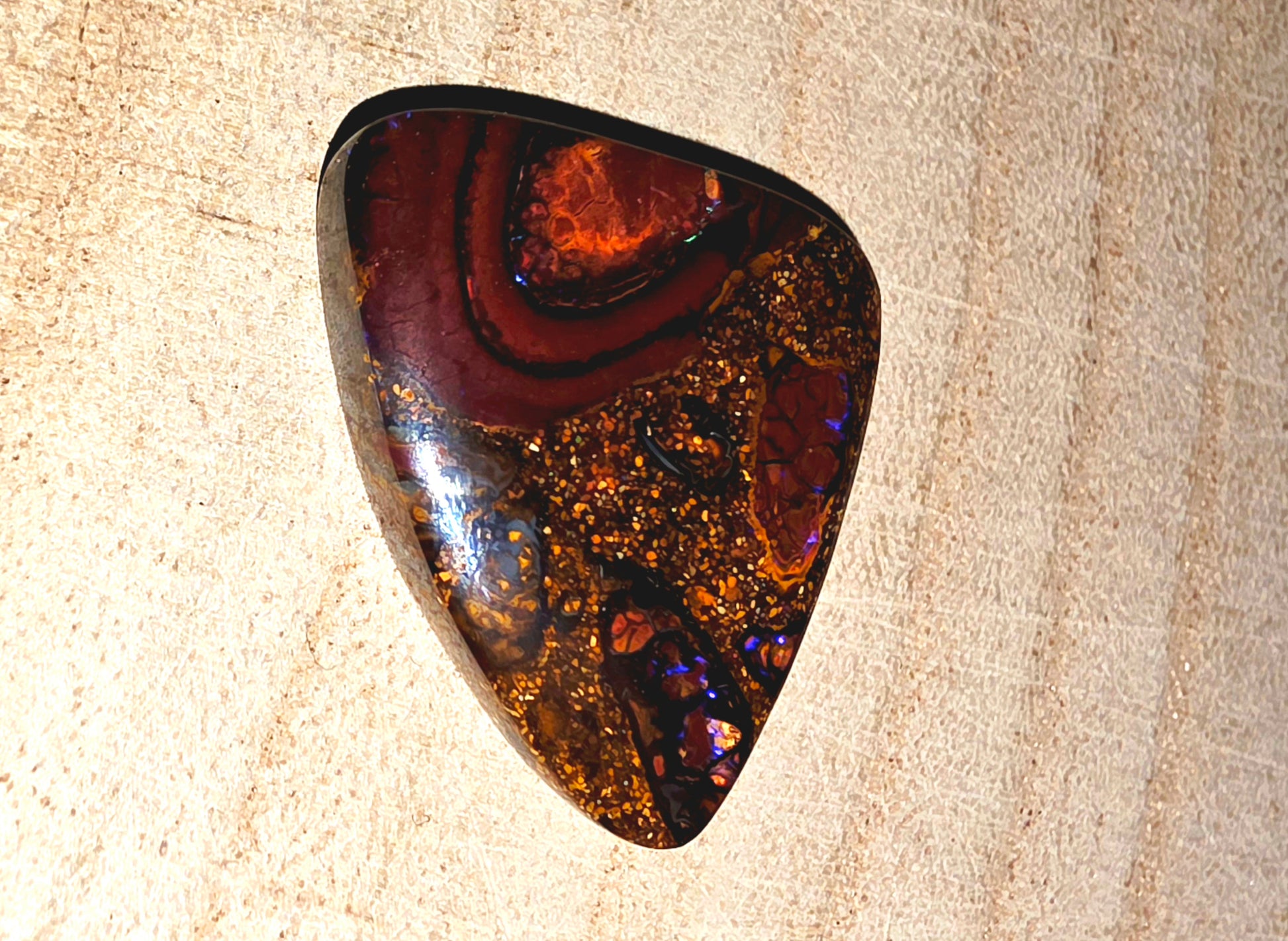Polished opal stone with brown and purple patterns on a beige surface