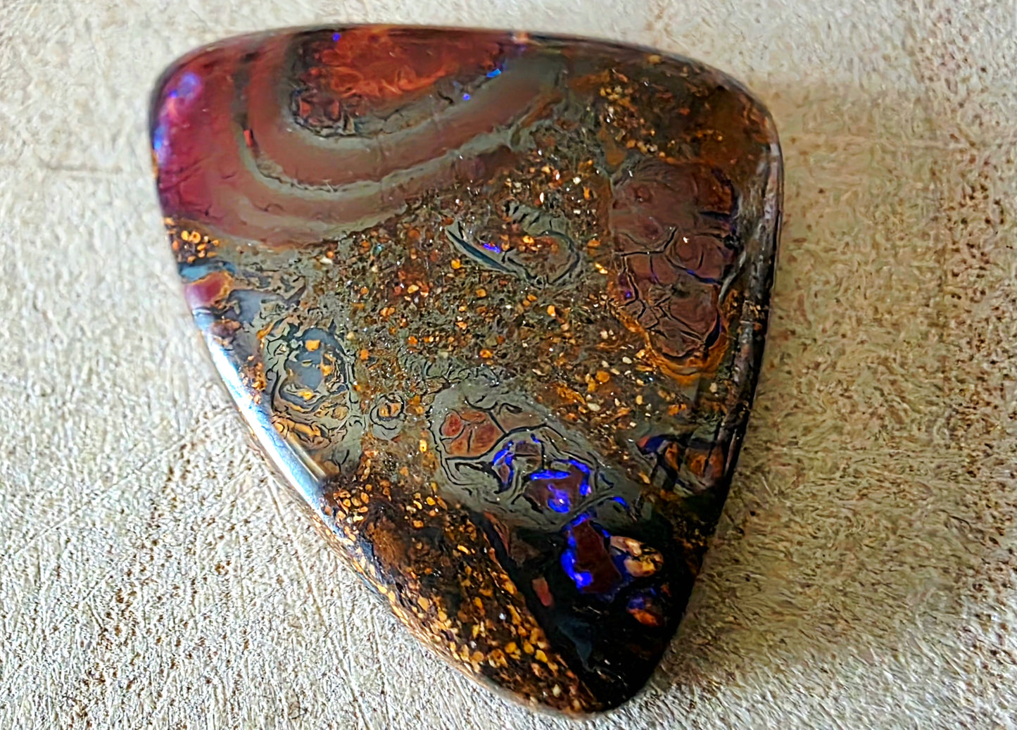 Polished opal with colourful patterns on a textured surface