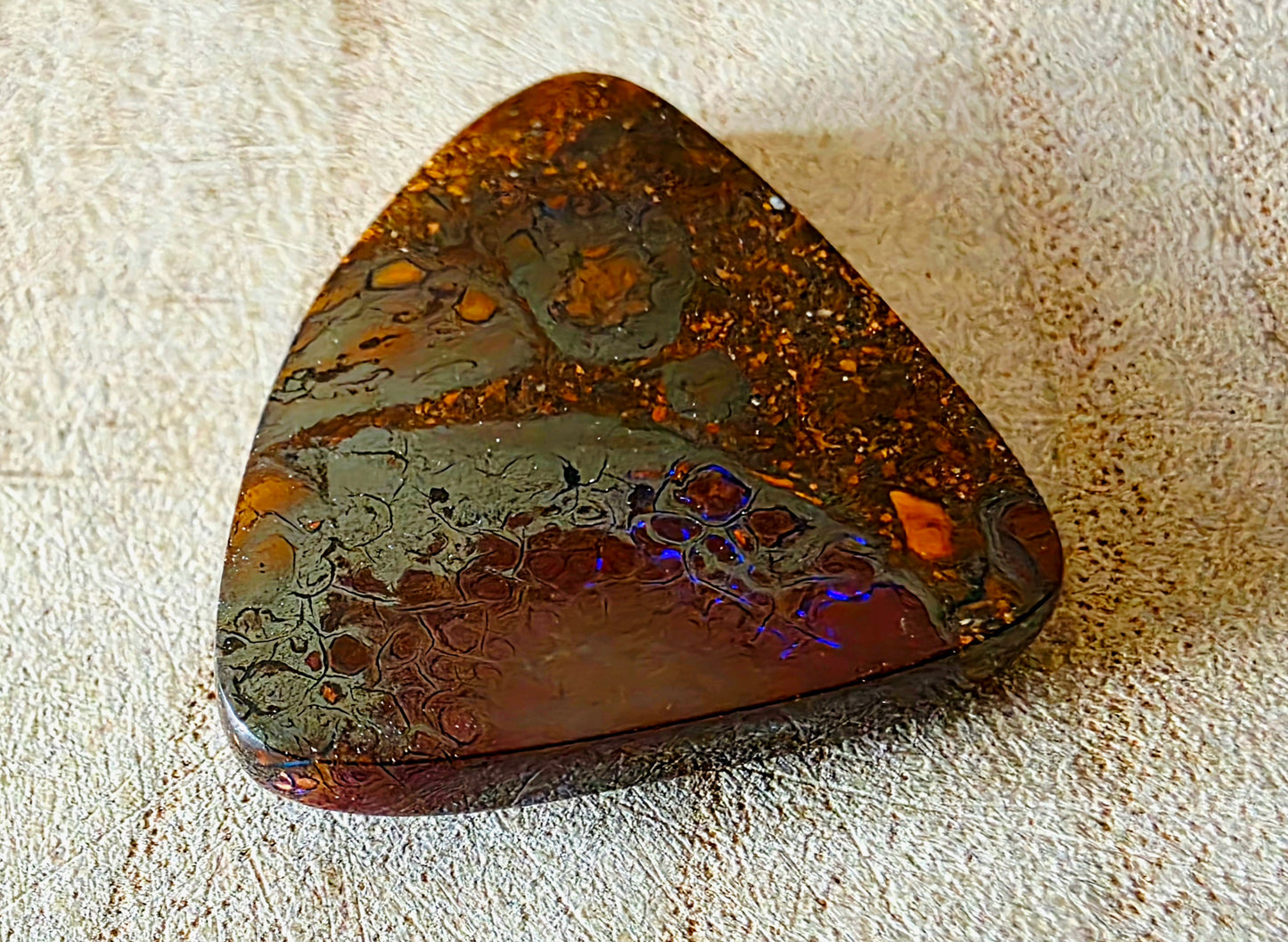Polished piece of opal material on a textured surface