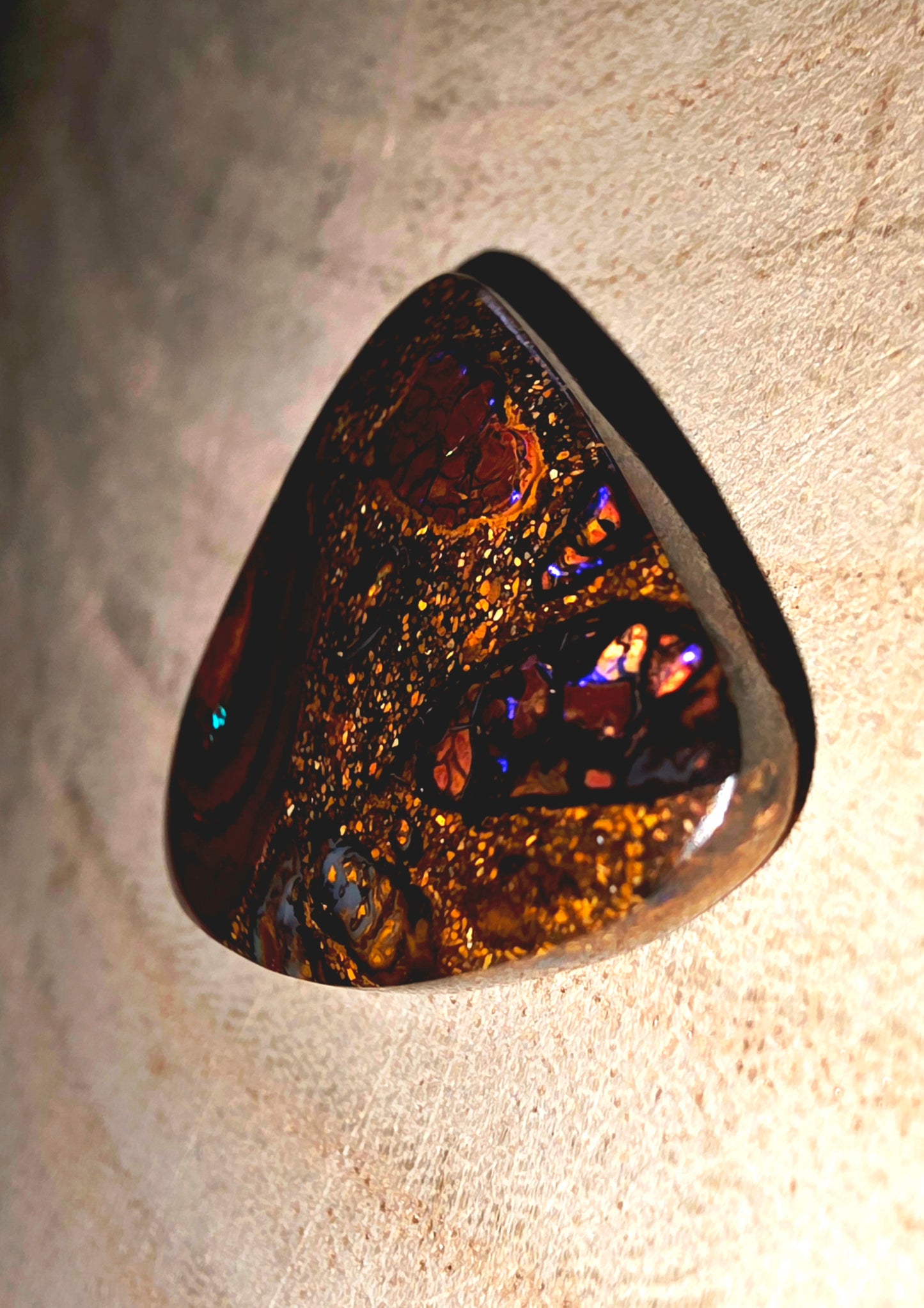 Triangular opal stone with multicoloured patterns on a textured surface
