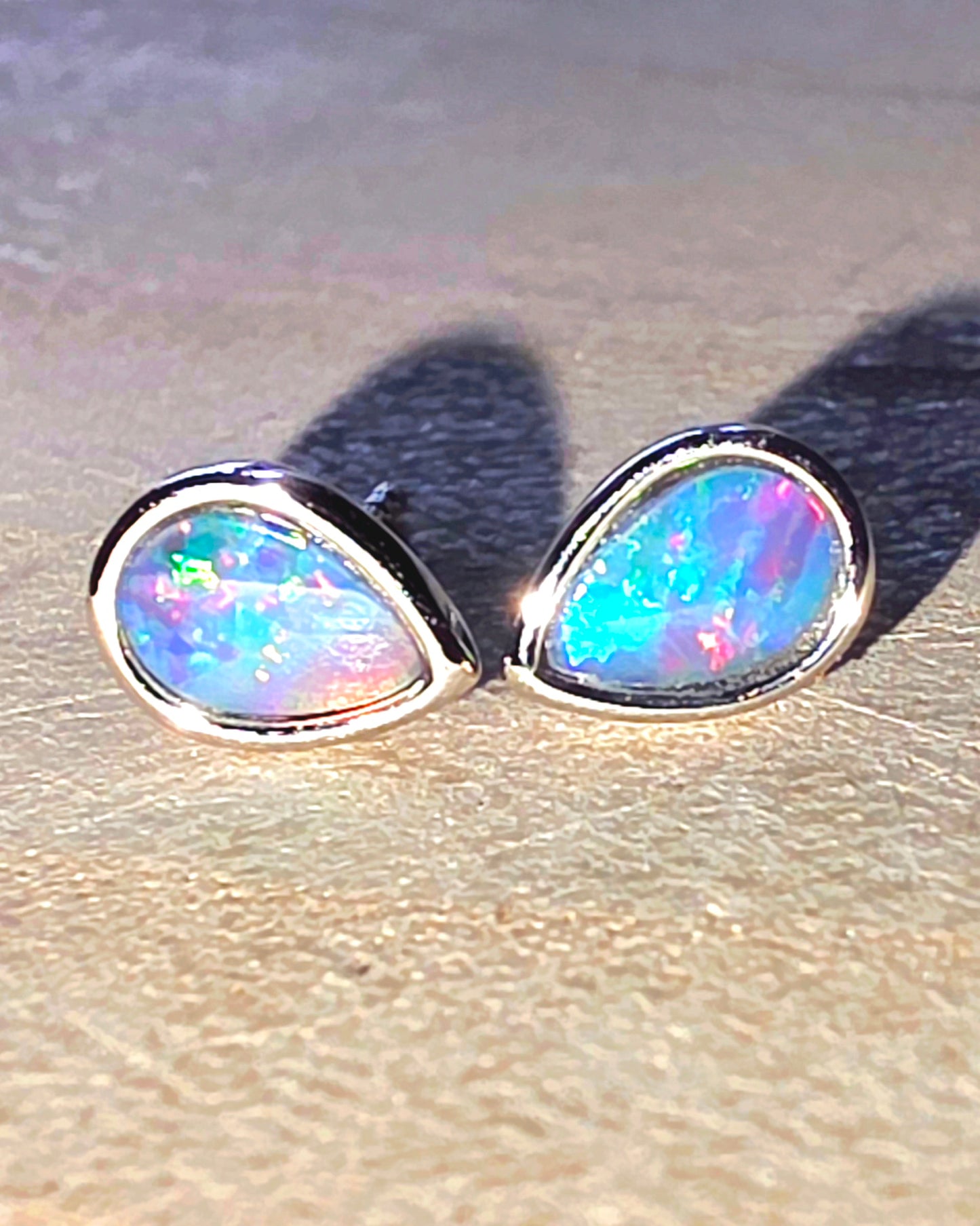 Opal stud earrings on a sandy surface