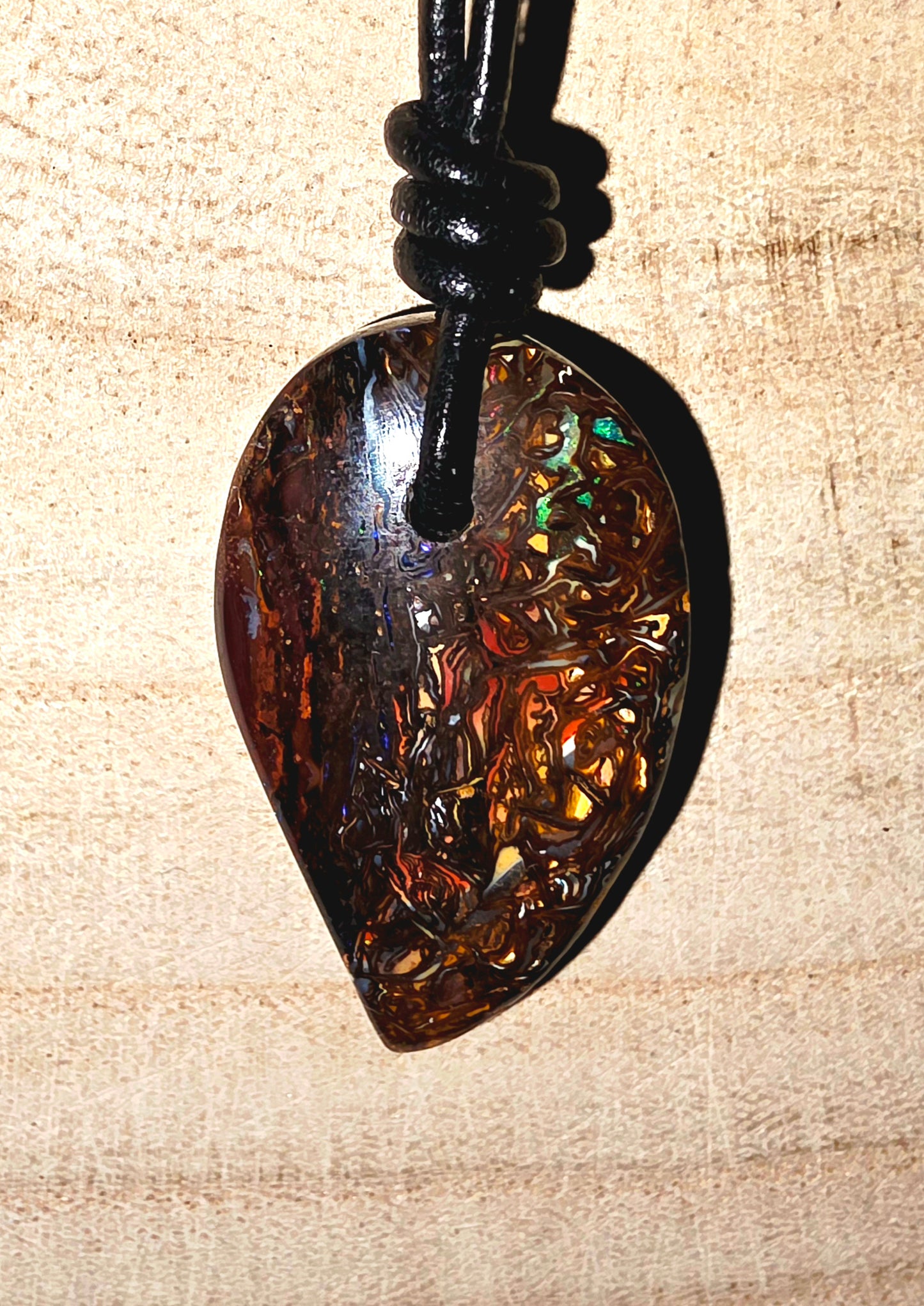 A teardrop-shaped amber pendant necklace with a black cord, displayed on a light wood background.