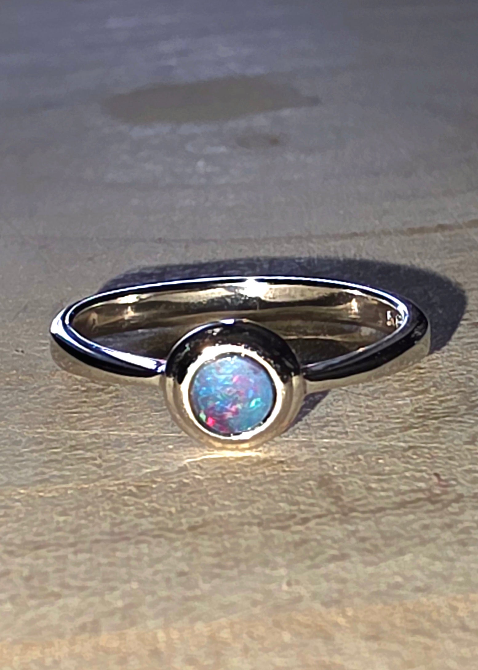 Silver opal ring with a central gemstone on a beige surface