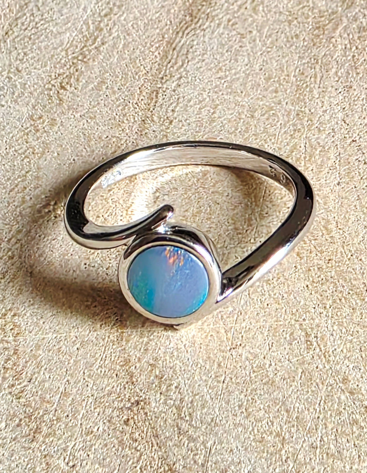 A sterling silver ring with a circular blue opal gemstone, photographed on a textured beige surface.