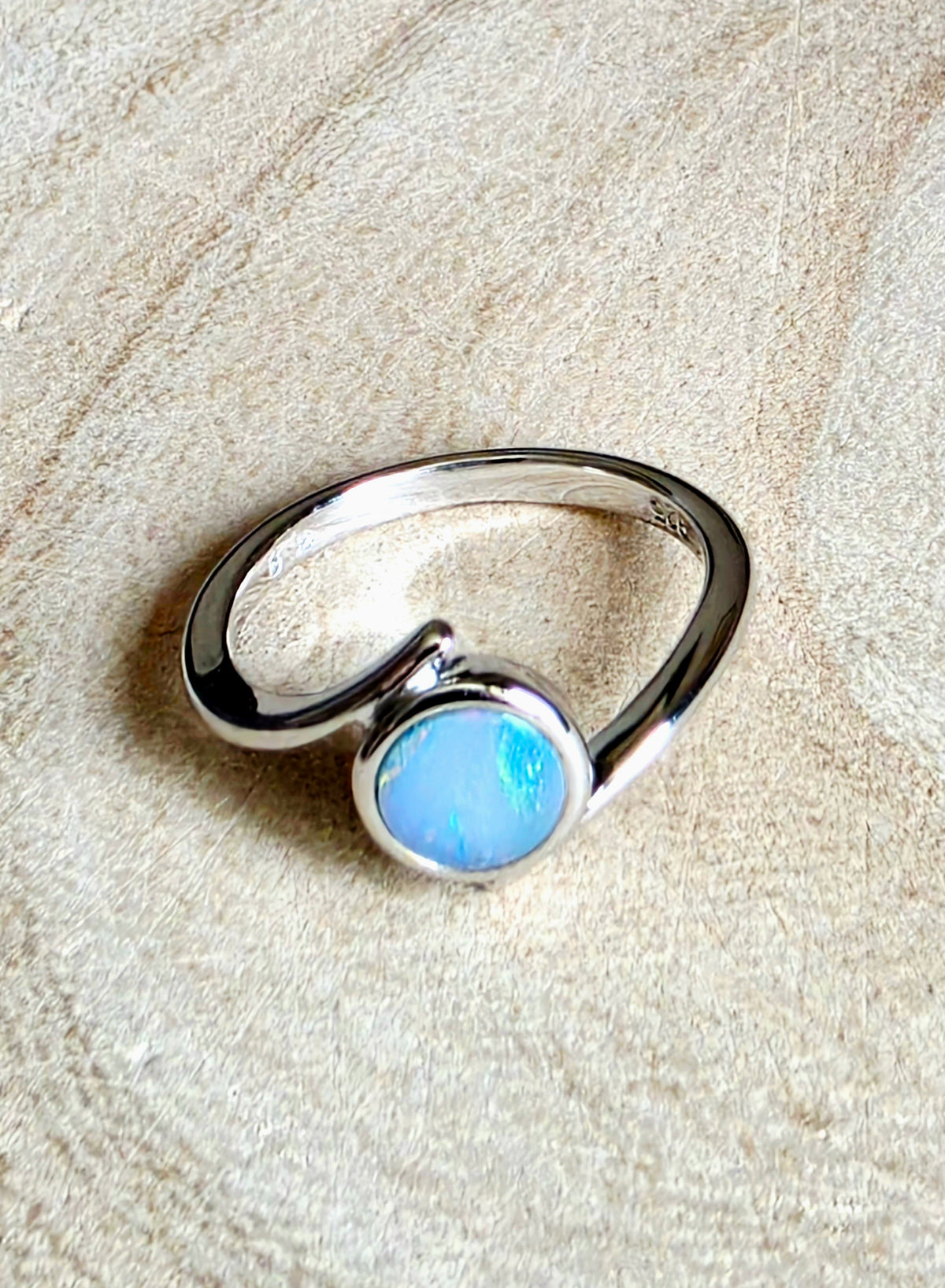 A sterling silver ring with a circular light blue opal gemstone, displayed on a textured beige fabric background.
