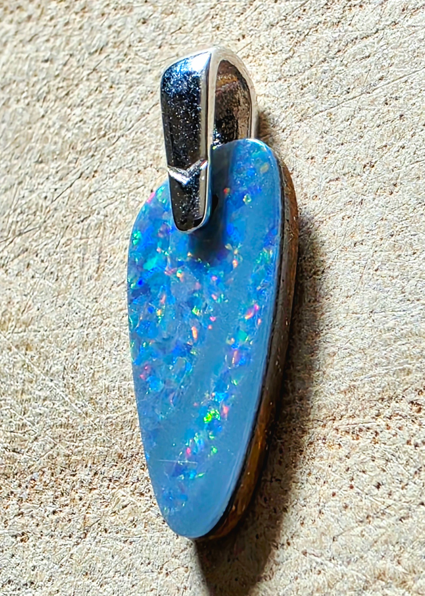 A blue opal pendant with a silver bail, resting on a textured beige surface.