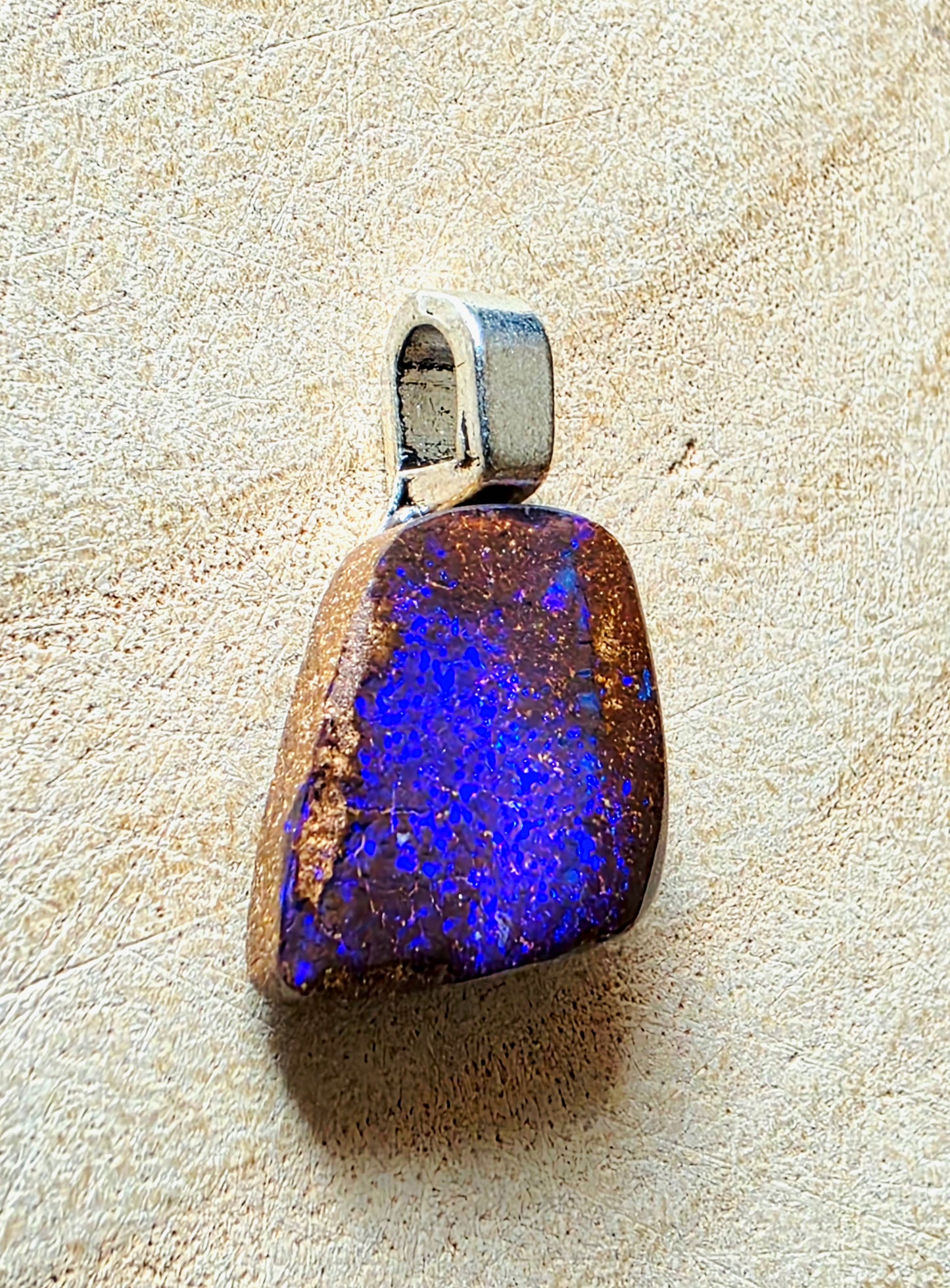 A natural blue opal pendant with a silver bail, resting on a textured beige surface.