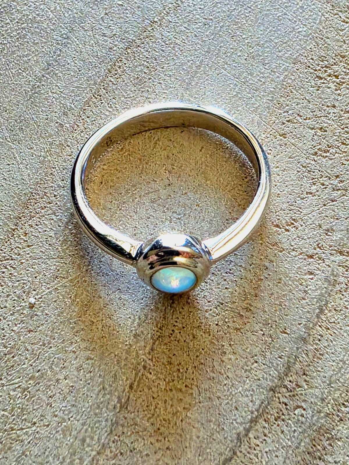 A 925 silver stacker ring with a crystal opal on a beige background