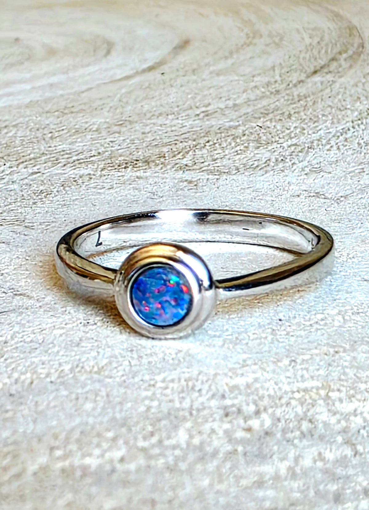 A silver ring featuring a round bezel-set blue opal gemstone, resting on a textured light beige fabric surface.