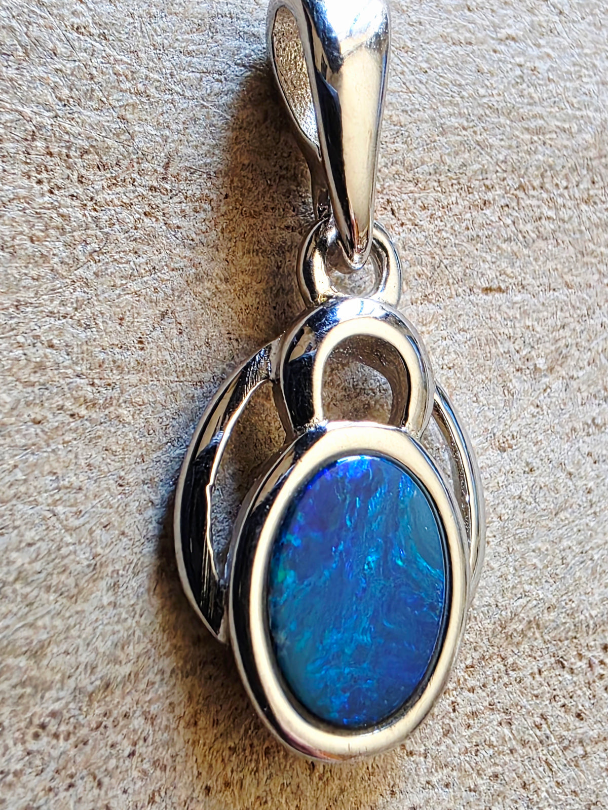 A sterling silver pendant featuring an oval blue opal stone, displayed on a textured beige surface.
