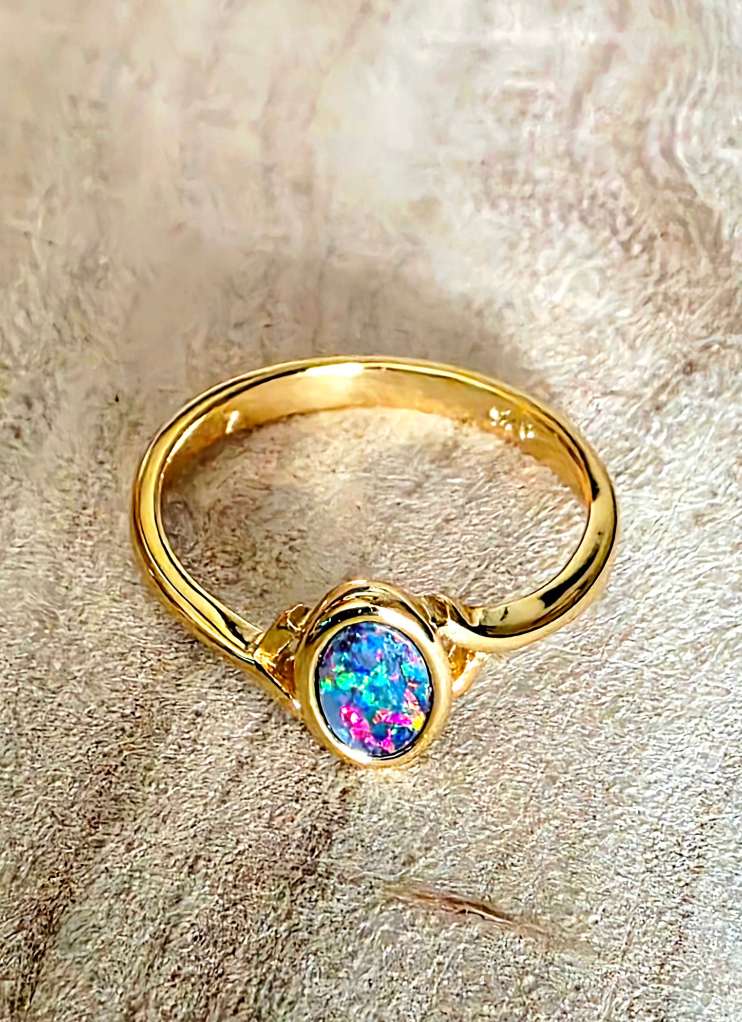 A gold ring with an oval iridescent opal gemstone, resting on a textured beige fabric background.
