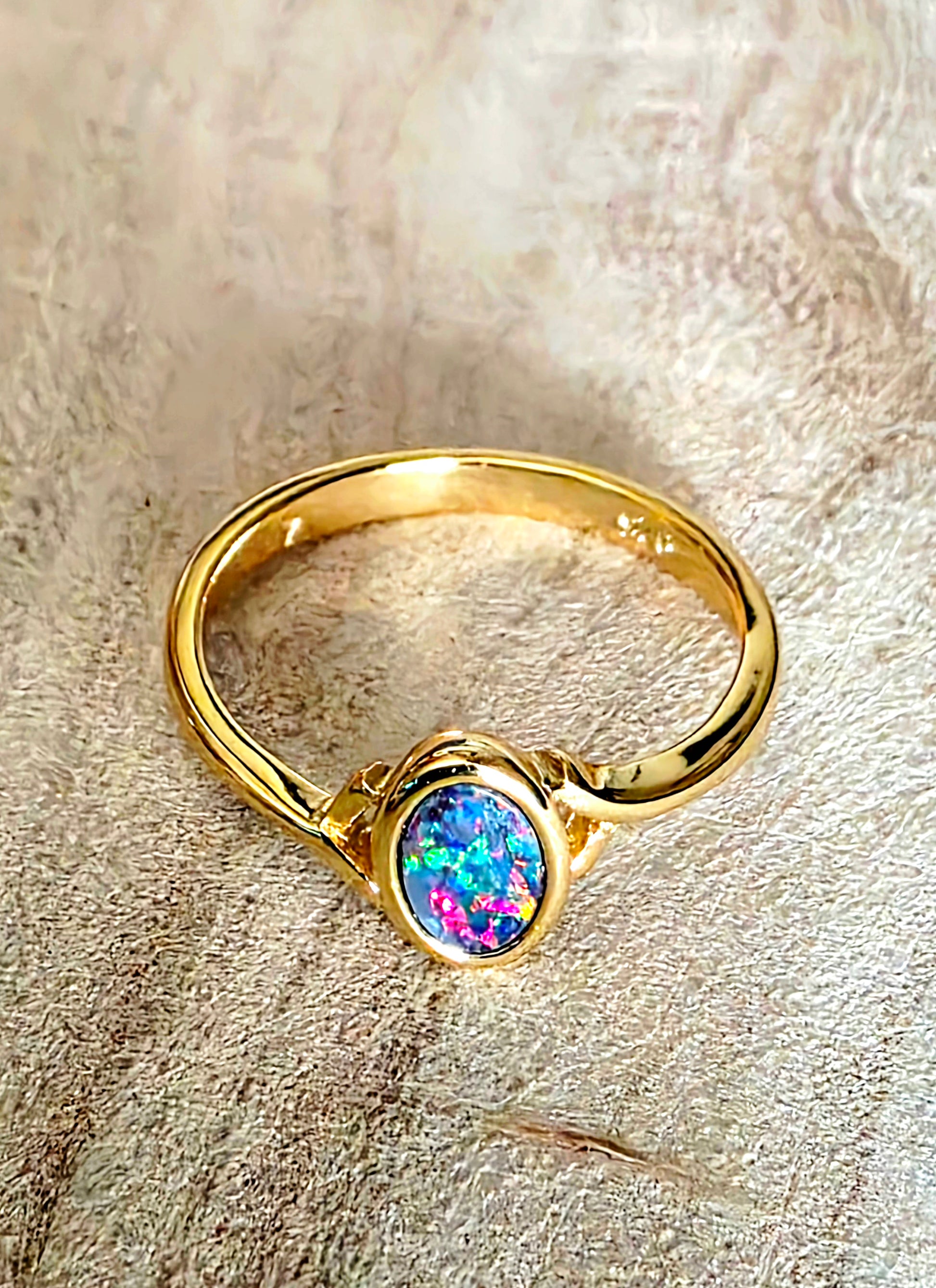 A gold ring with an oval iridescent opal gemstone, resting on a textured beige fabric background.