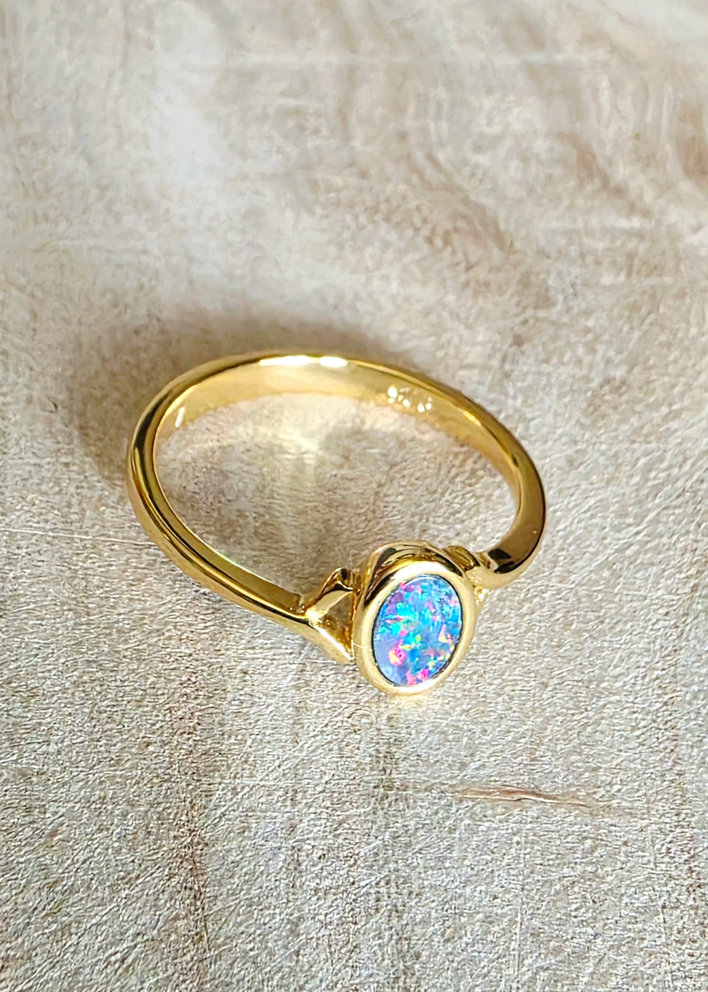 A gold ring featuring an oval-cut iridescent opal gemstone, resting on a textured beige fabric background.