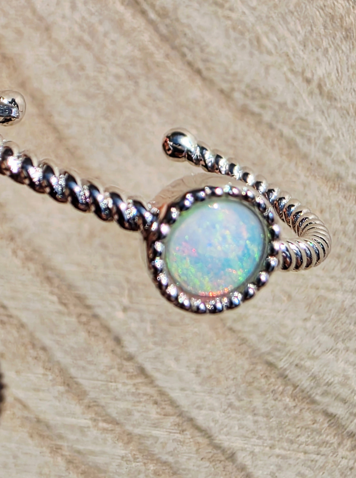 A silver twisted band ring featuring a round iridescent opal gemstone in a beaded bezel setting, displayed on a textured beige fur background.
